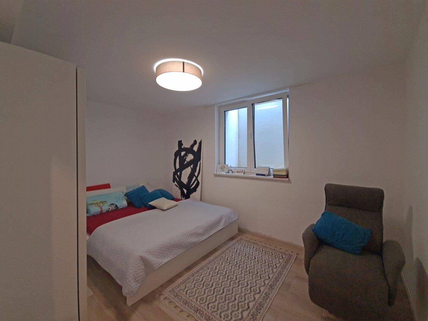 Schlafzimmer mit Doppelbett, Fenster und moderner Wanddekoration.
