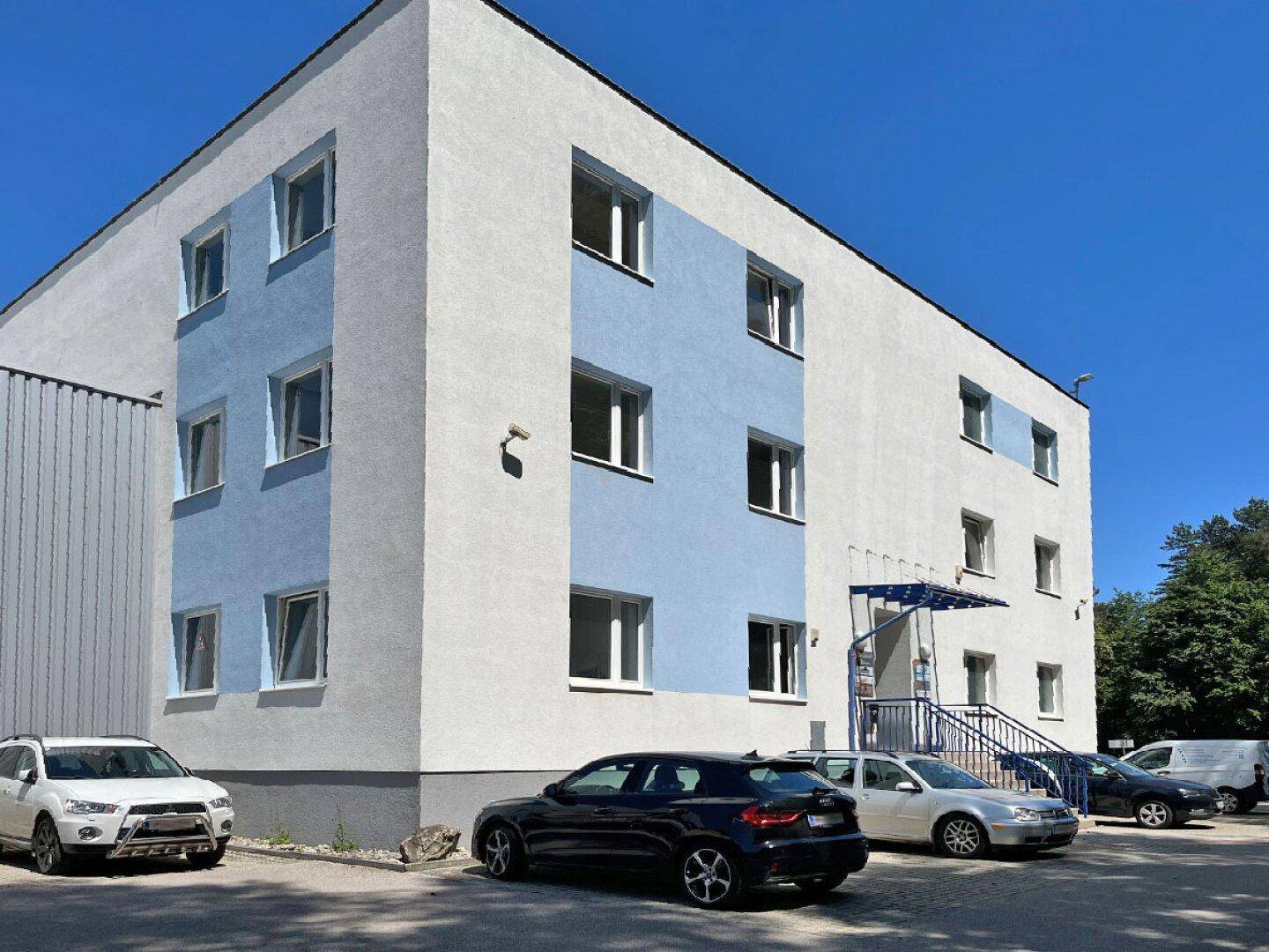 Modernes Geschäftsgebäude mit blauen Akzenten und Parkplätzen unter strahlend blauem Himmel.
