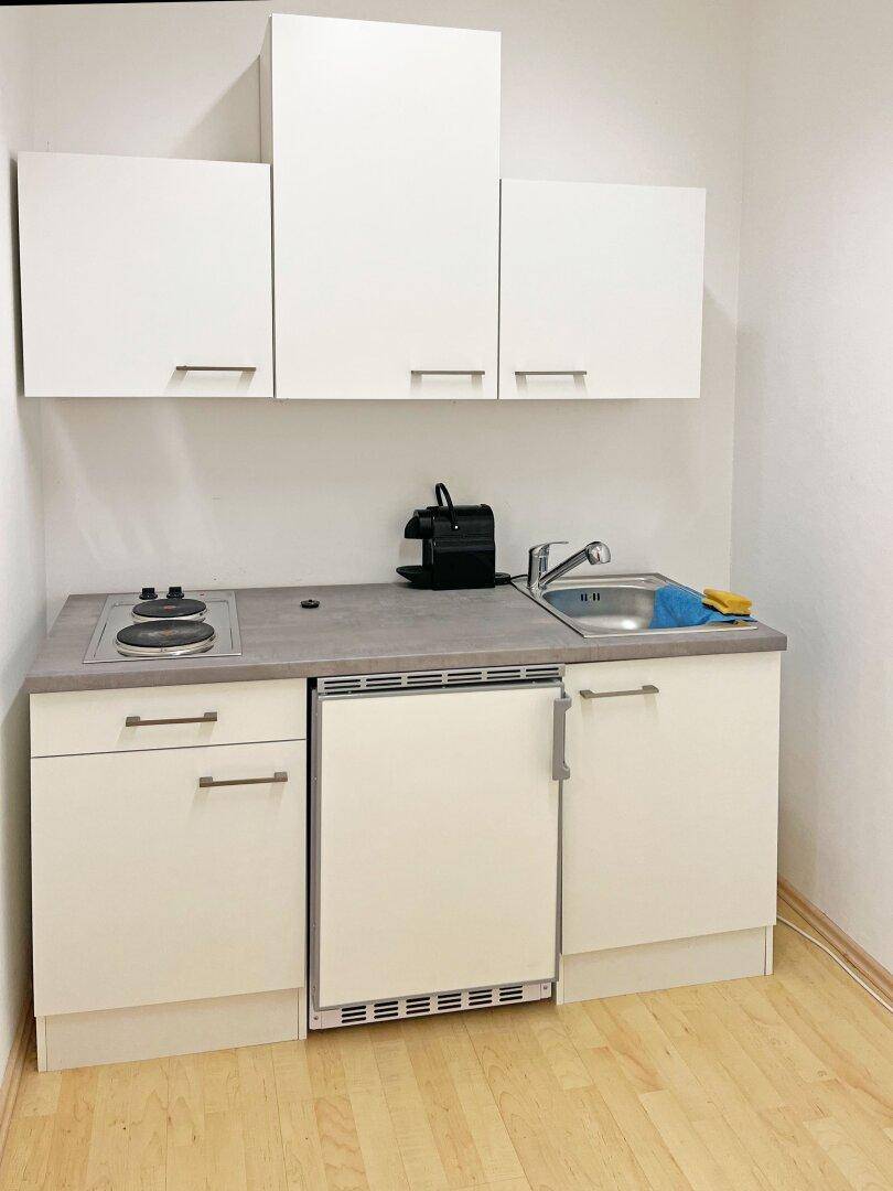 Kompakte, weiße Teeküche mit Spüle, Kochfeld und integriertem Kühlschrank, ideal für kleine Büros.