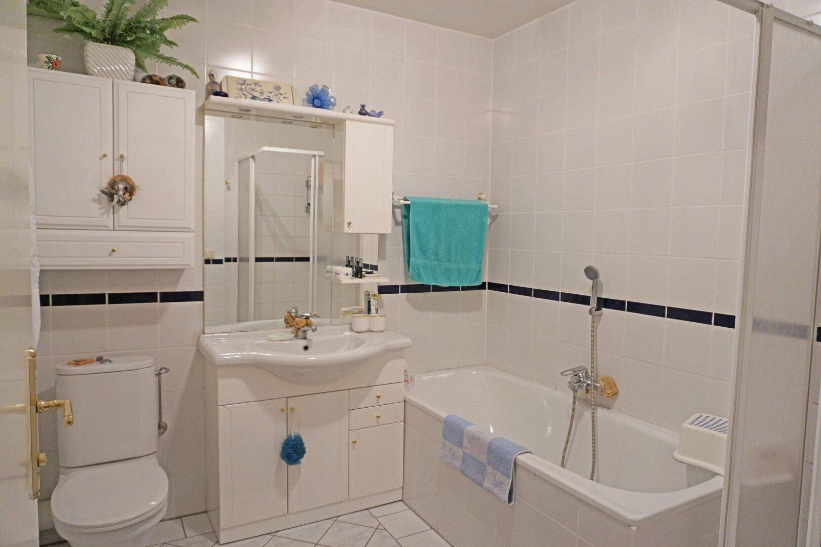 Gefliestes Badezimmer in Weiß mit Badewanne, Dusche und Waschtisch.