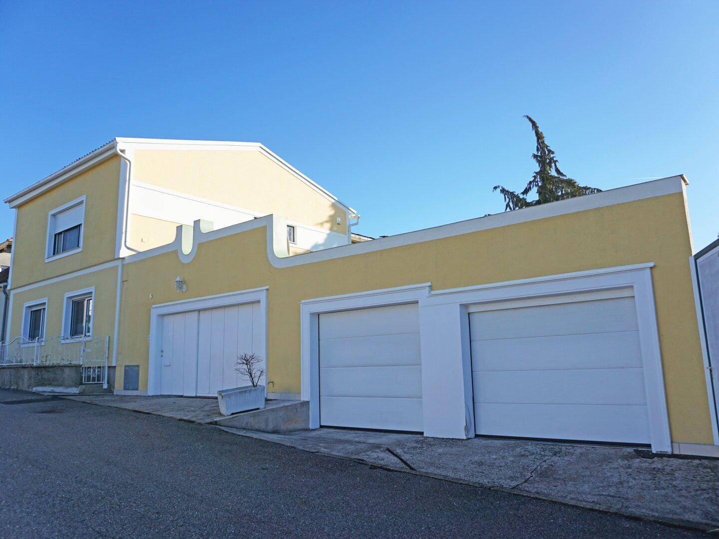 Gelbe Hausfassade mit mehreren Garagentoren und weißer Putzverzierung unter blauem Himmel.