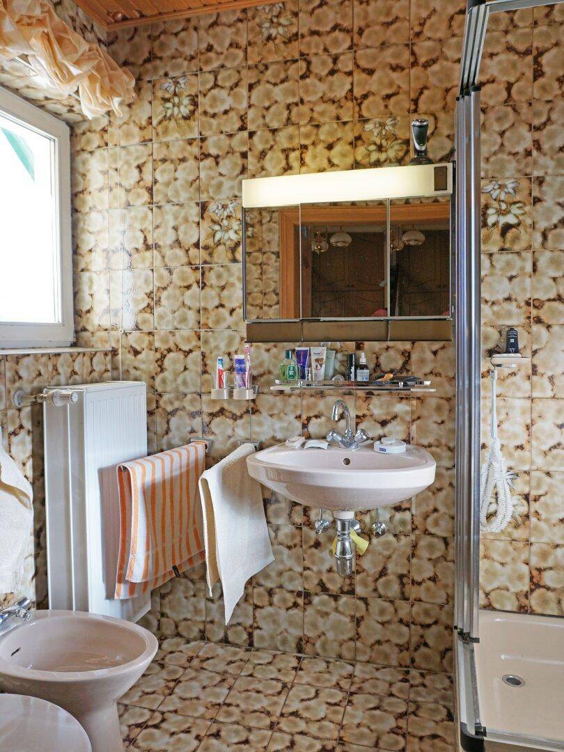 Badezimmer im 80er-Jahre-Stil mit gemusterten Fliesen, Waschbecken, Bidet und Duschkabine.