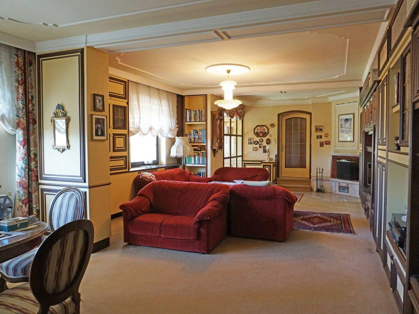 Geräumiges Wohnzimmer mit roten Sofas, Teppichboden und dekorativer Stuckdecke.