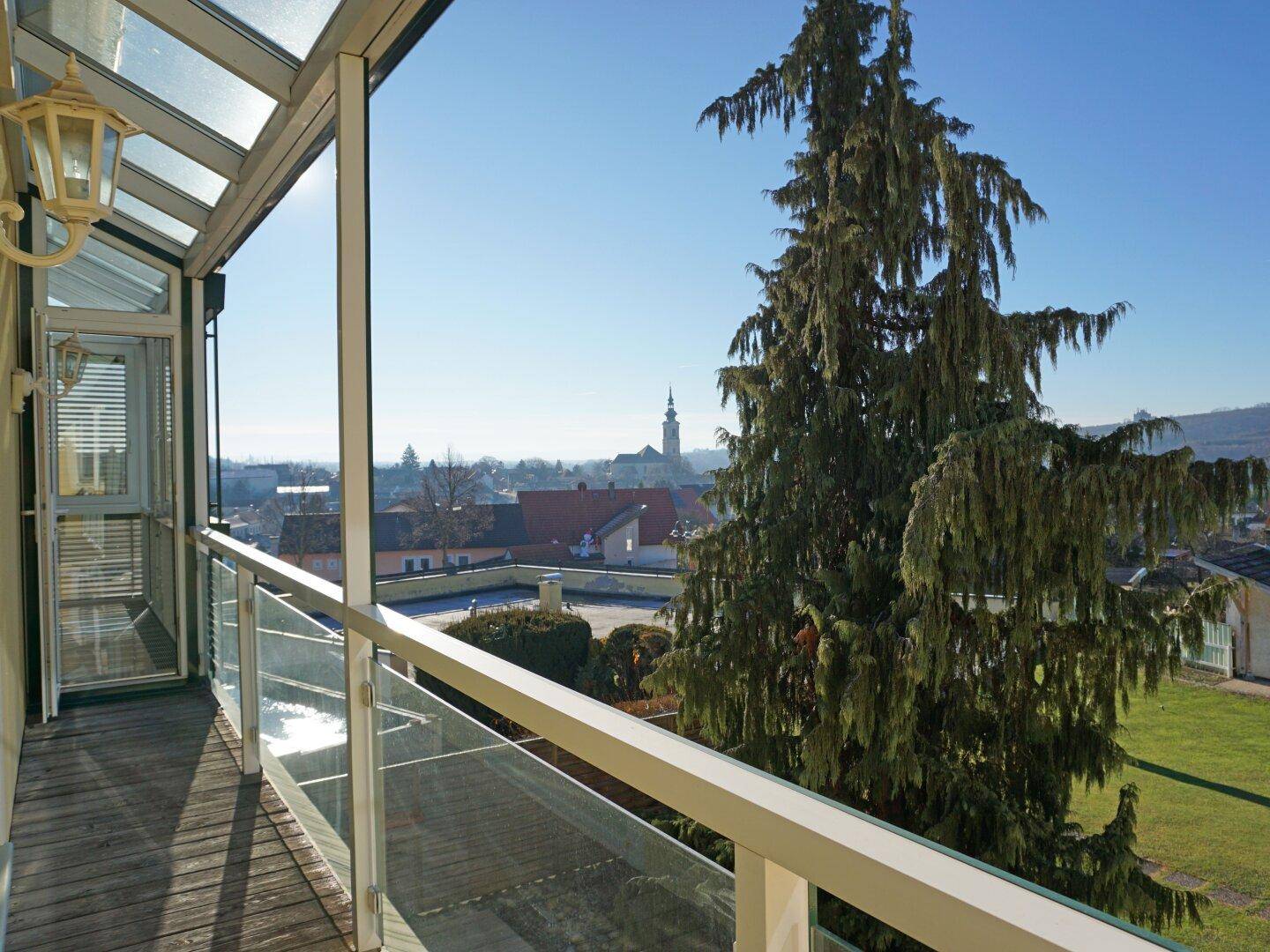 Überdachte Loggia mit Holzboden, Glasgeländer und weitem Blick über die Stadt.