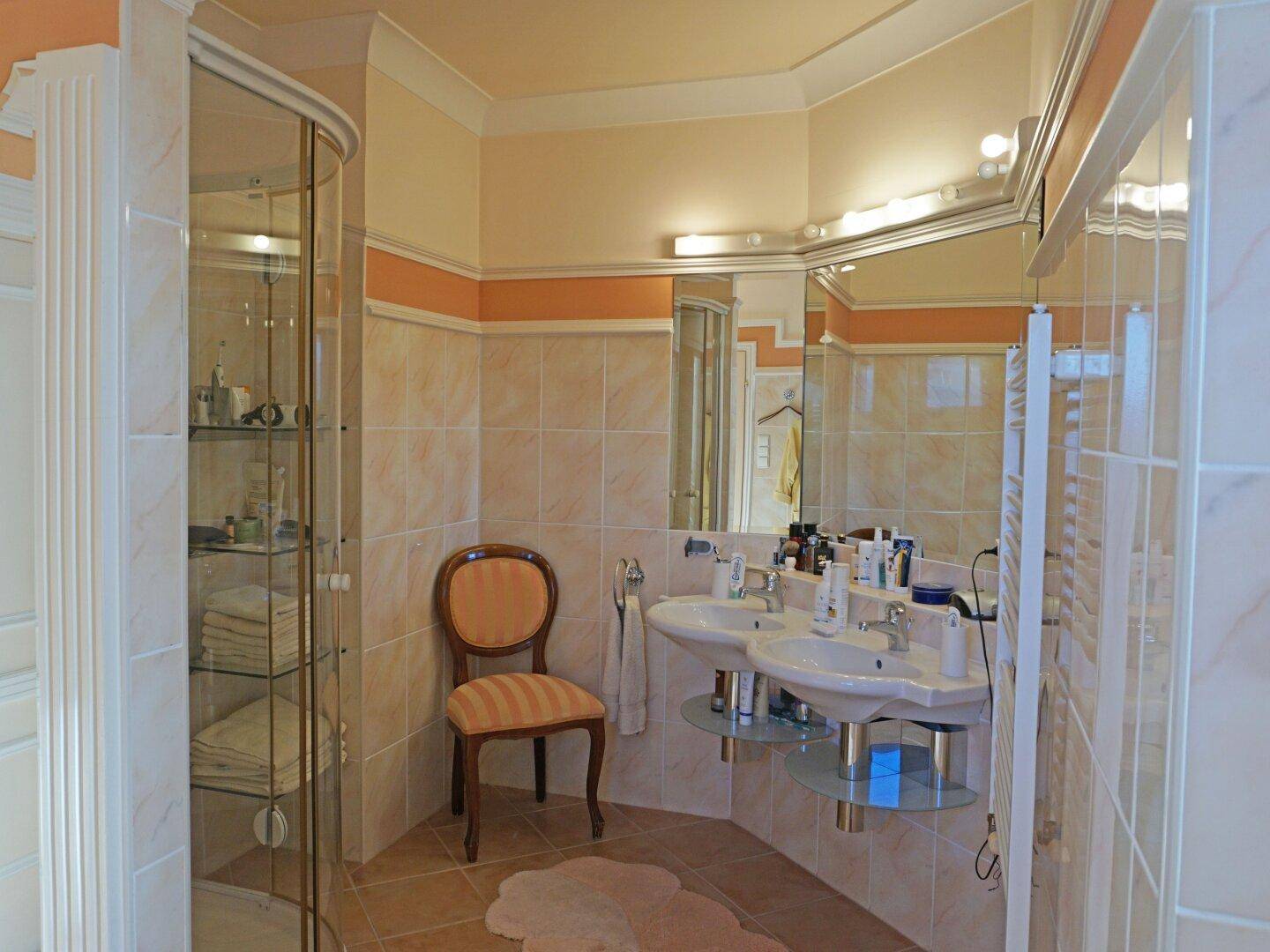Elegantes Badezimmer mit Doppelwaschbecken, Duschkabine und hellen Fliesen.