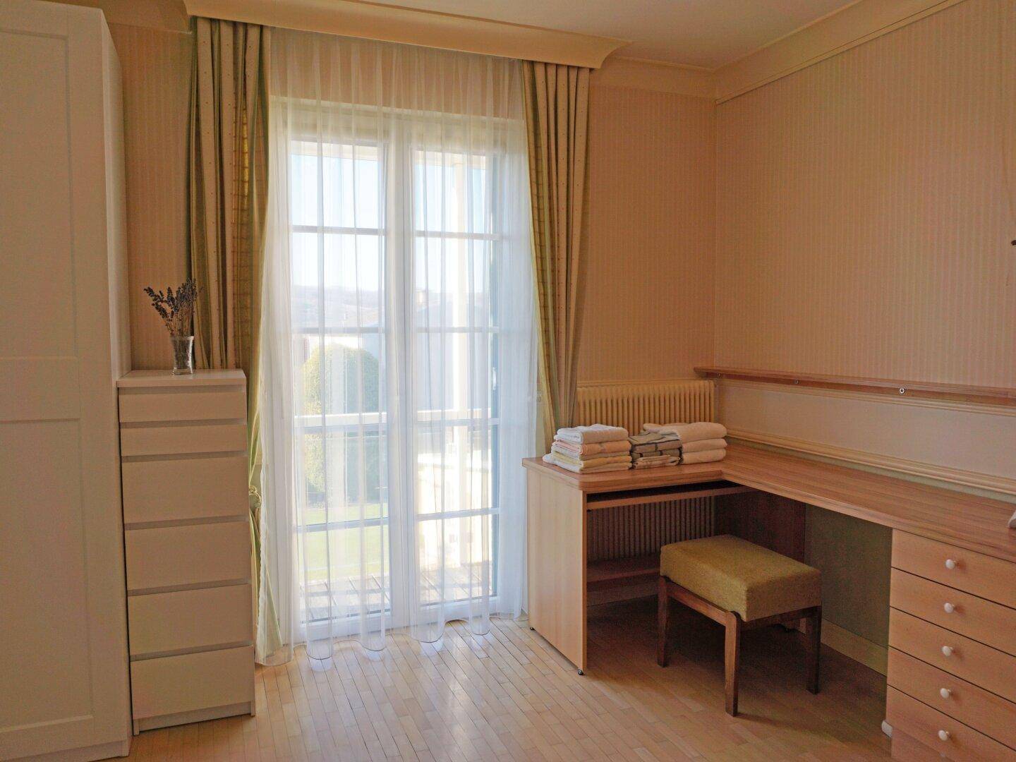 Helles Zimmer mit Holzboden, Schreibtisch und Zugang zu einem Balkon oder Garten.