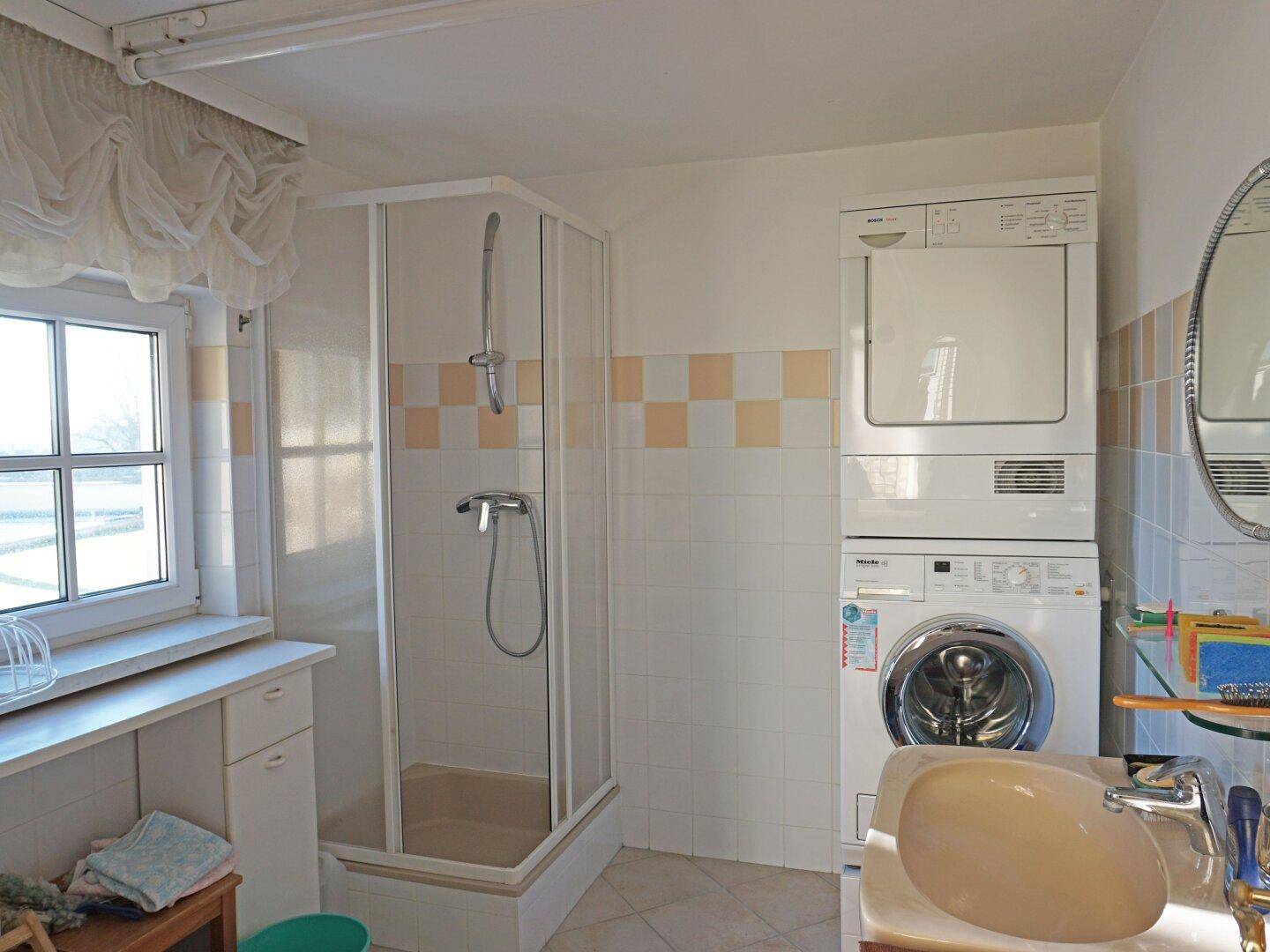 Helles Badezimmer mit Duschkabine, Waschmaschine und Trockner sowie Fenster.
