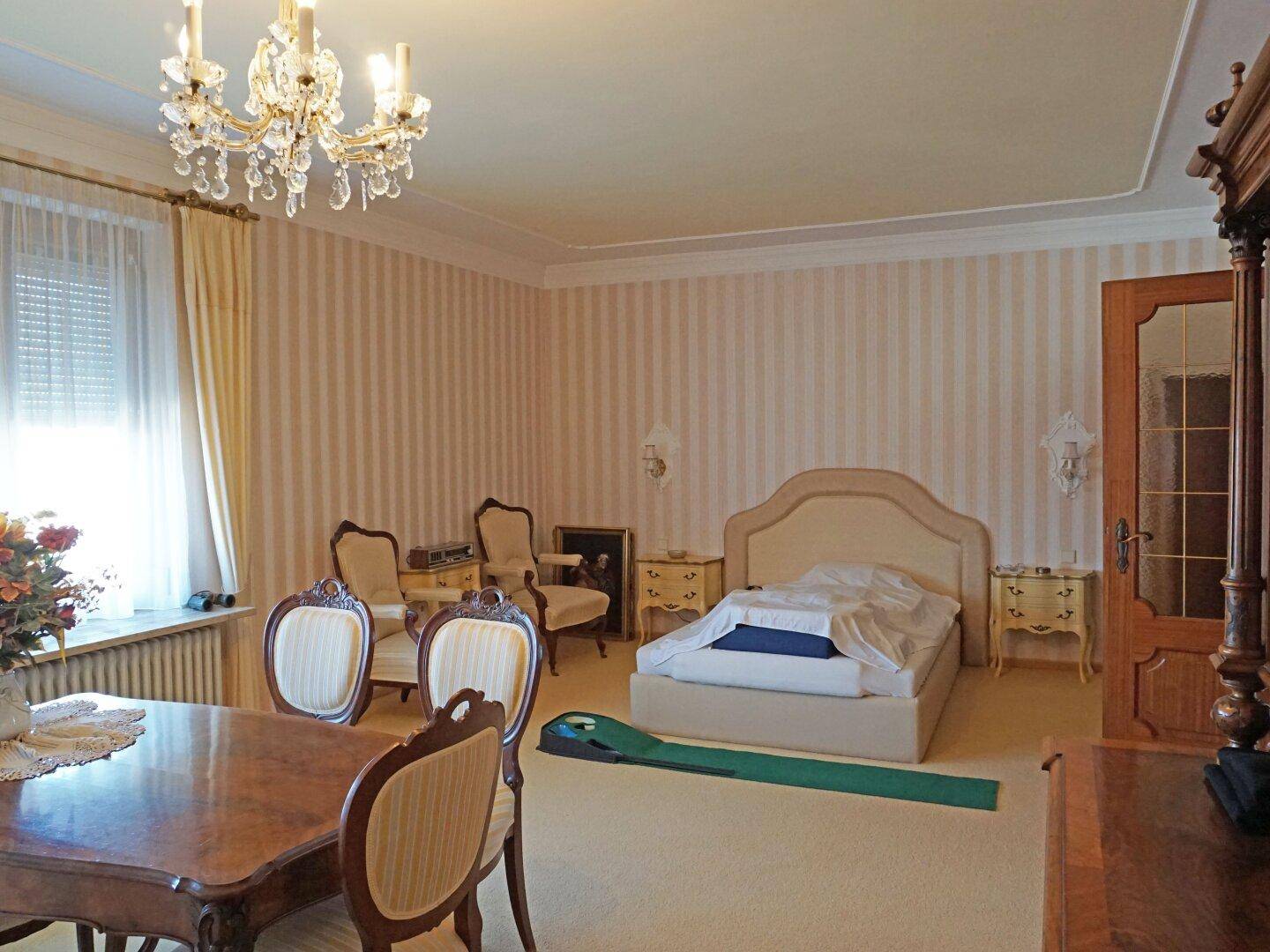 Klassisches Schlafzimmer mit Teppichboden, großem Bett und Kronleuchter.