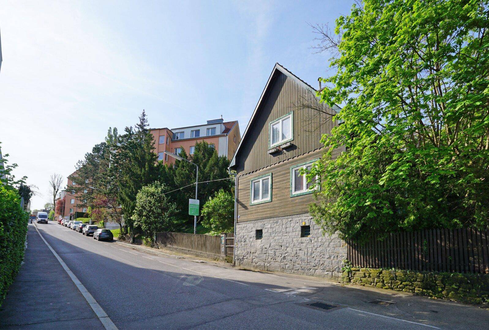 Seitenansicht des Hauses mit Holzfassade und Steinsockel, entlang einer ruhigen Straße gelegen.