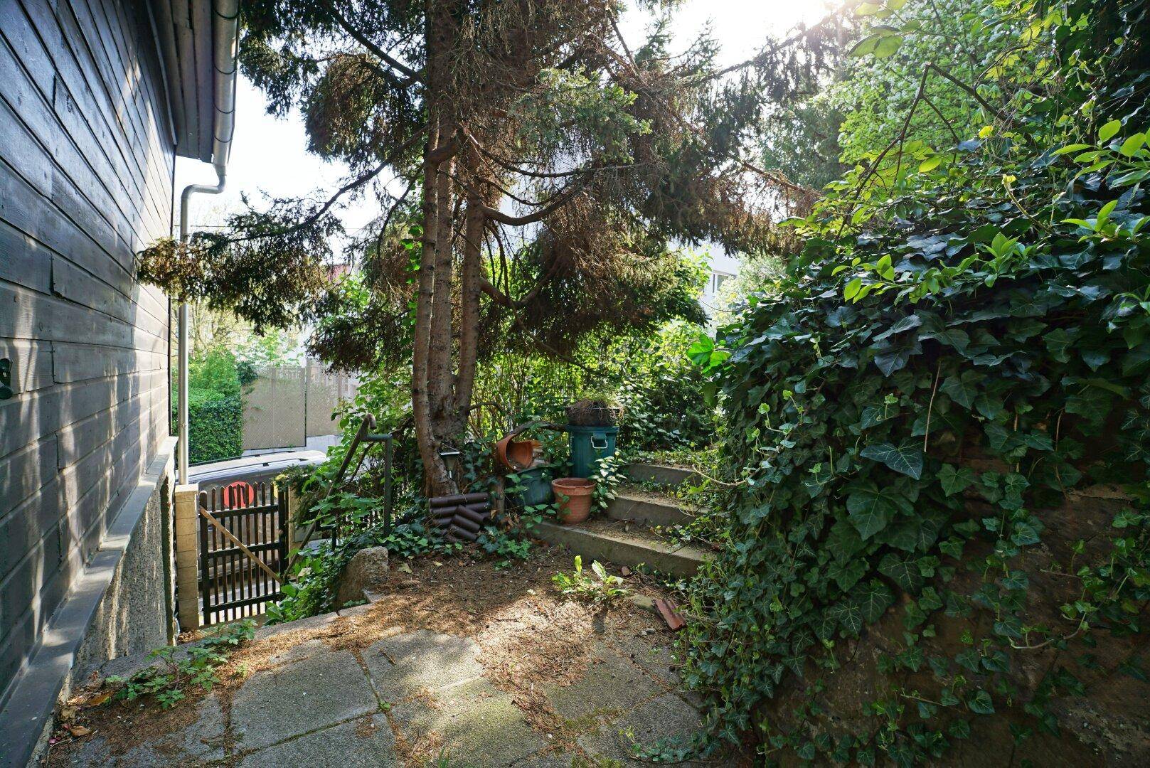 Gartenbereich mit Steinstufen und üppiger Vegetation, neben dem Haus gelegen.