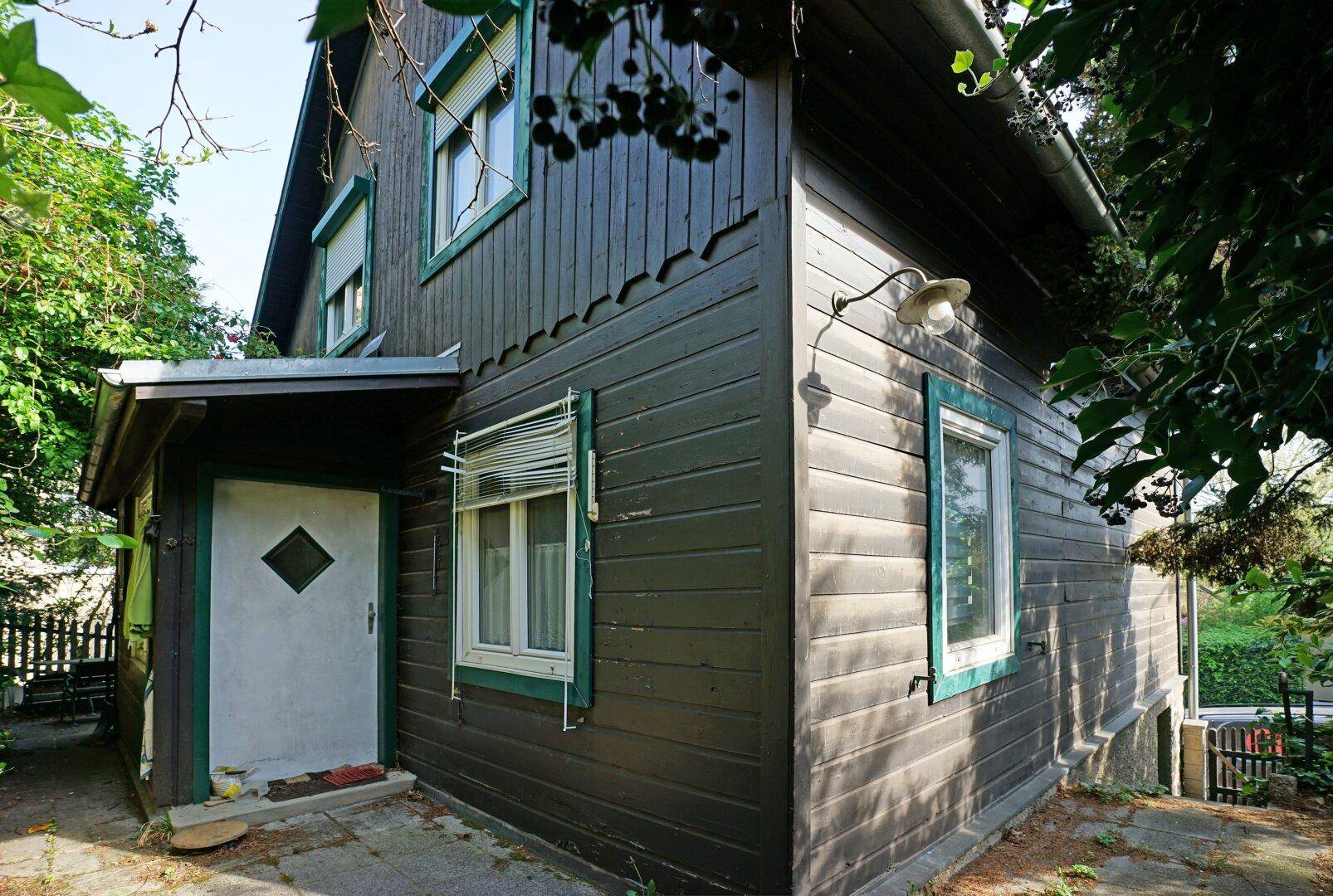 Ecke des Hauses mit Holzfassade, Fenstern und einem überdachten Eingangsbereich.