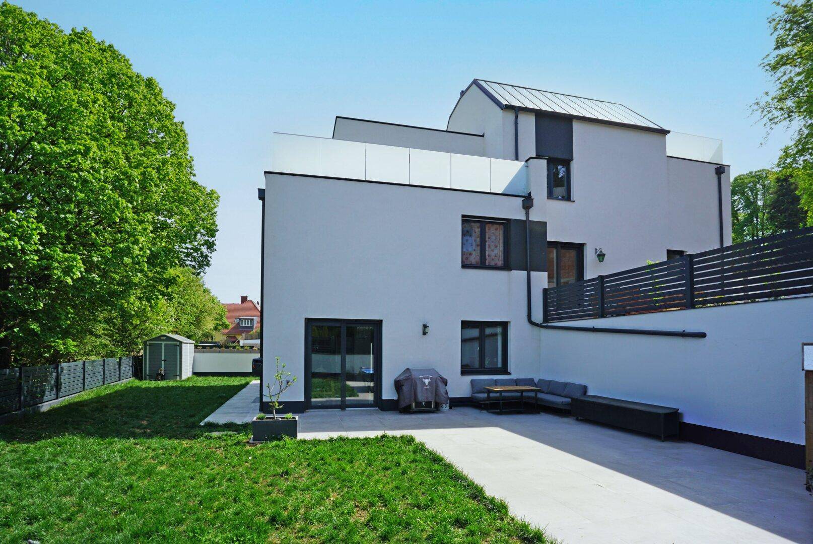 Hinterhofbereich mit gepflasterter Terrasse, bequemen Gartenmöbeln und einem kleinen Rasen.