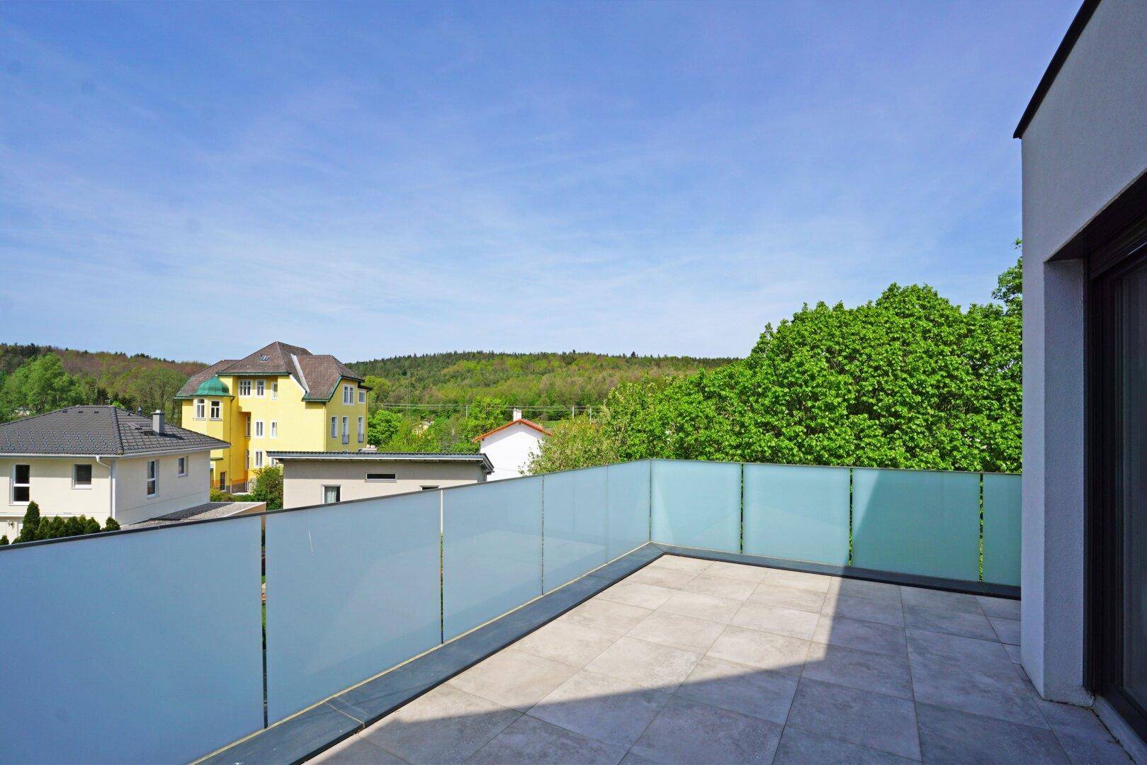 Großer Balkon mit Fliesenboden und Milchglasgeländer, bietet weite Aussicht ins Grüne.
