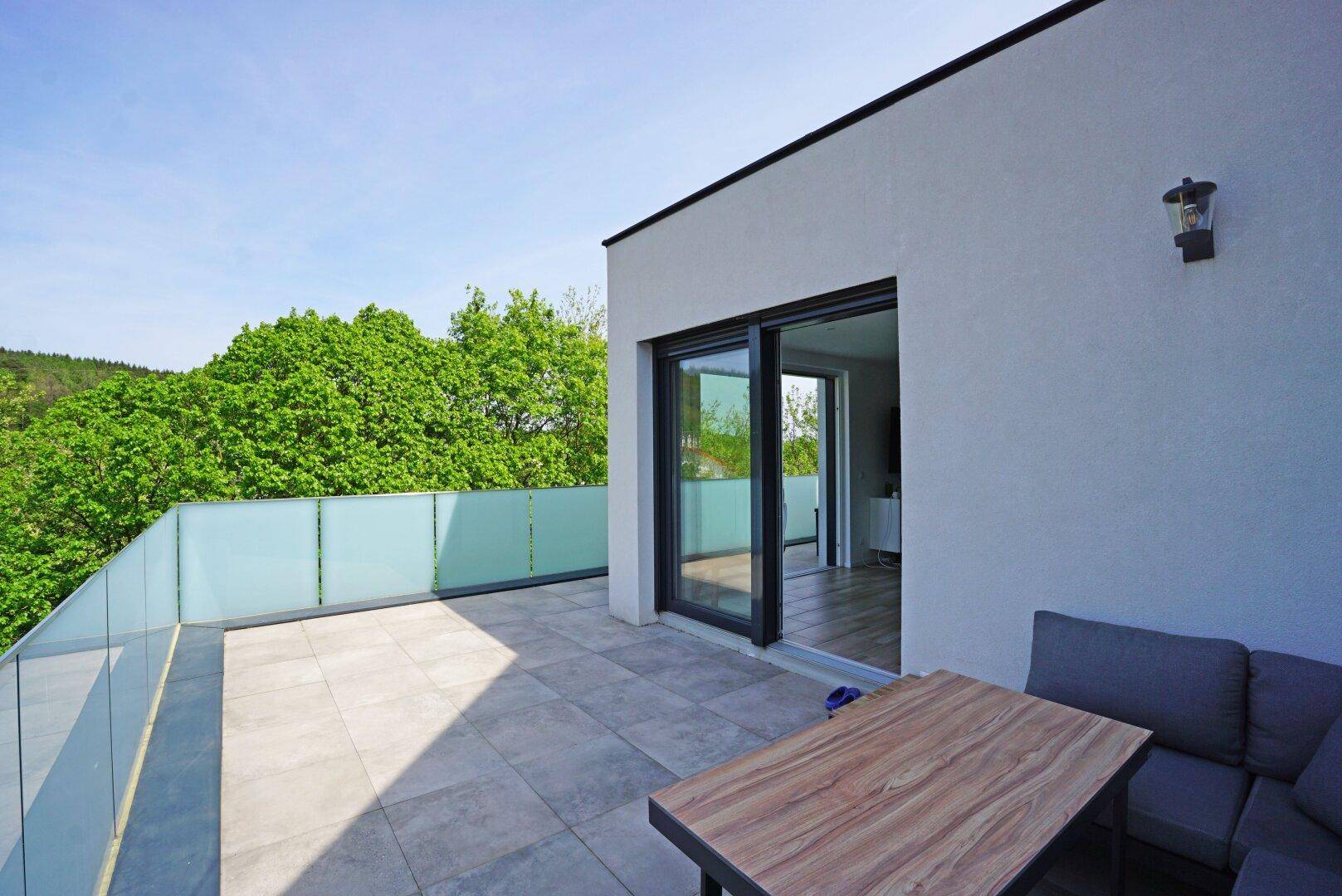 Helle Terrasse mit Fliesenboden, bequemen Sitzgelegenheiten und weitem Blick ins Grüne.