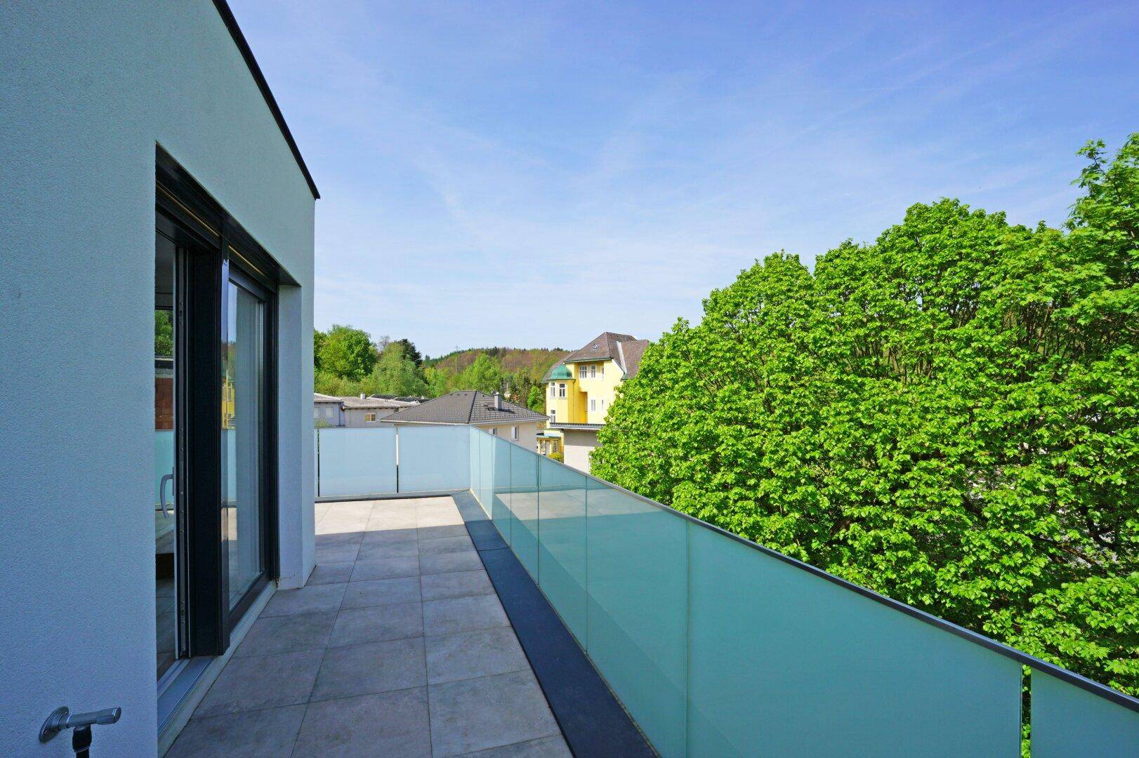 Langer Balkon mit Fliesenboden und Milchglasgeländer, bietet einen schönen Blick auf die Natur.