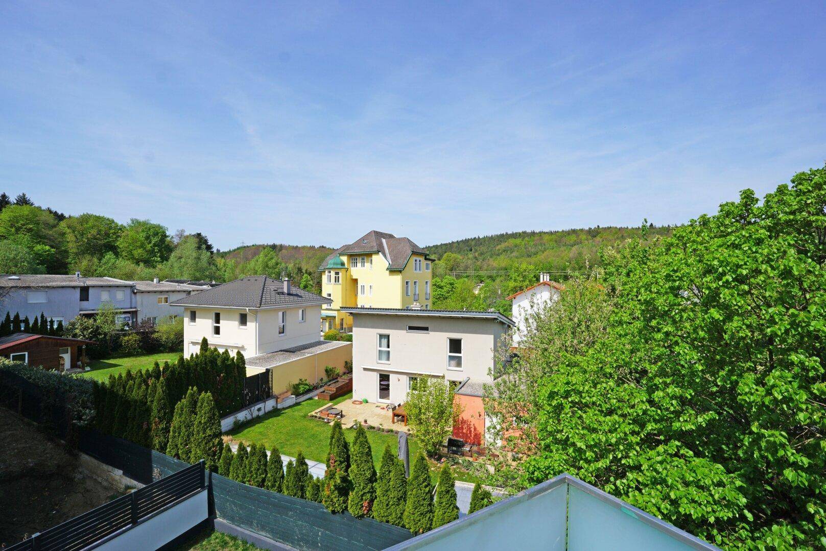 Weitläufiger Ausblick über eine Wohnsiedlung mit viel Grün und bewaldeten Hügeln im Hintergrund.
