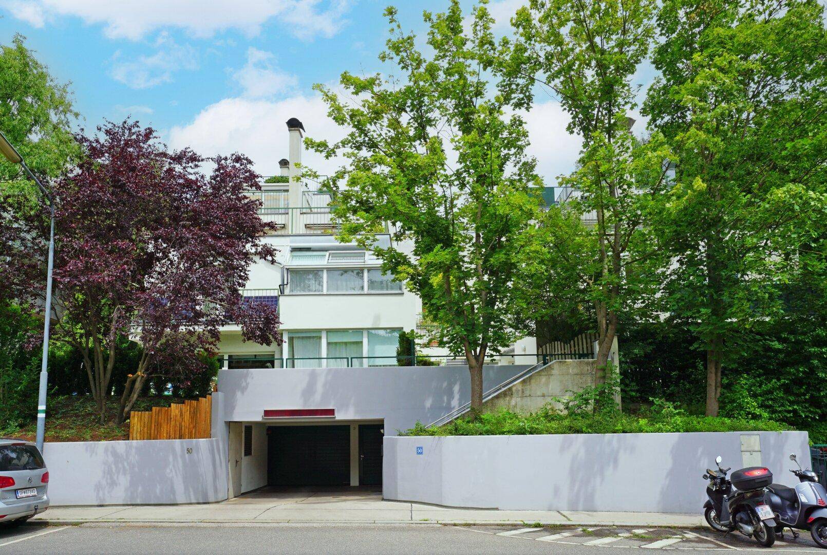 Moderne Wohnanlage mit Tiefgaragenzufahrt, umgeben von Bäumen und Grünflächen.