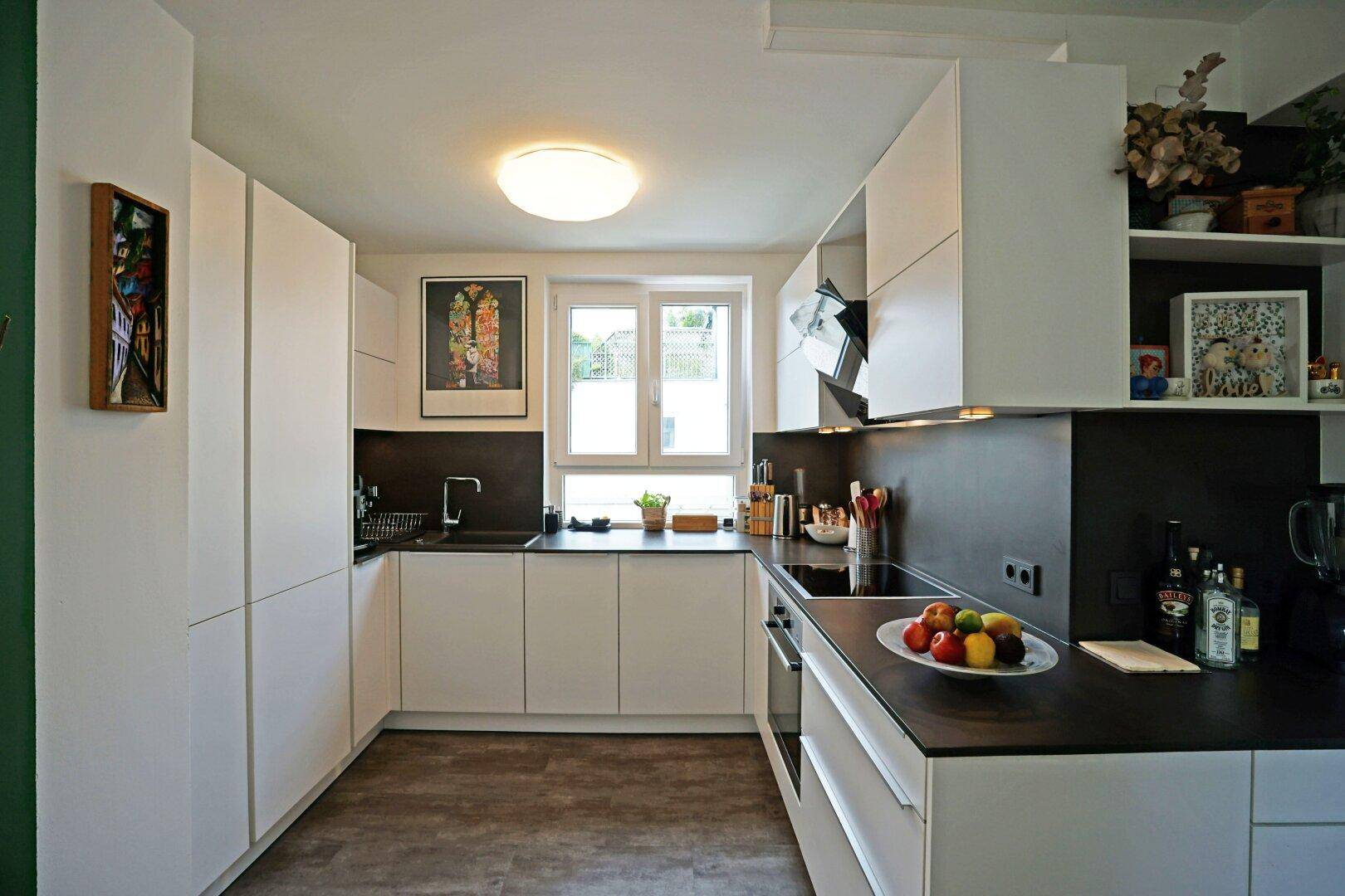 Moderne weiße Einbauküche mit dunklen Arbeitsplatten, Fenster und integrierten Geräten.