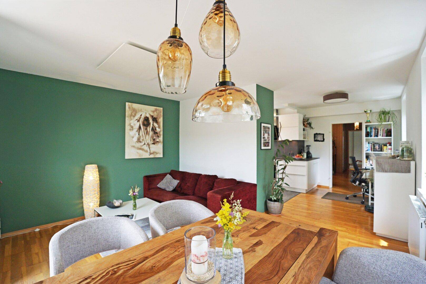 Gemütlicher Wohn-Essbereich mit Holztisch, rotem Sofa und grüner Akzentwand.