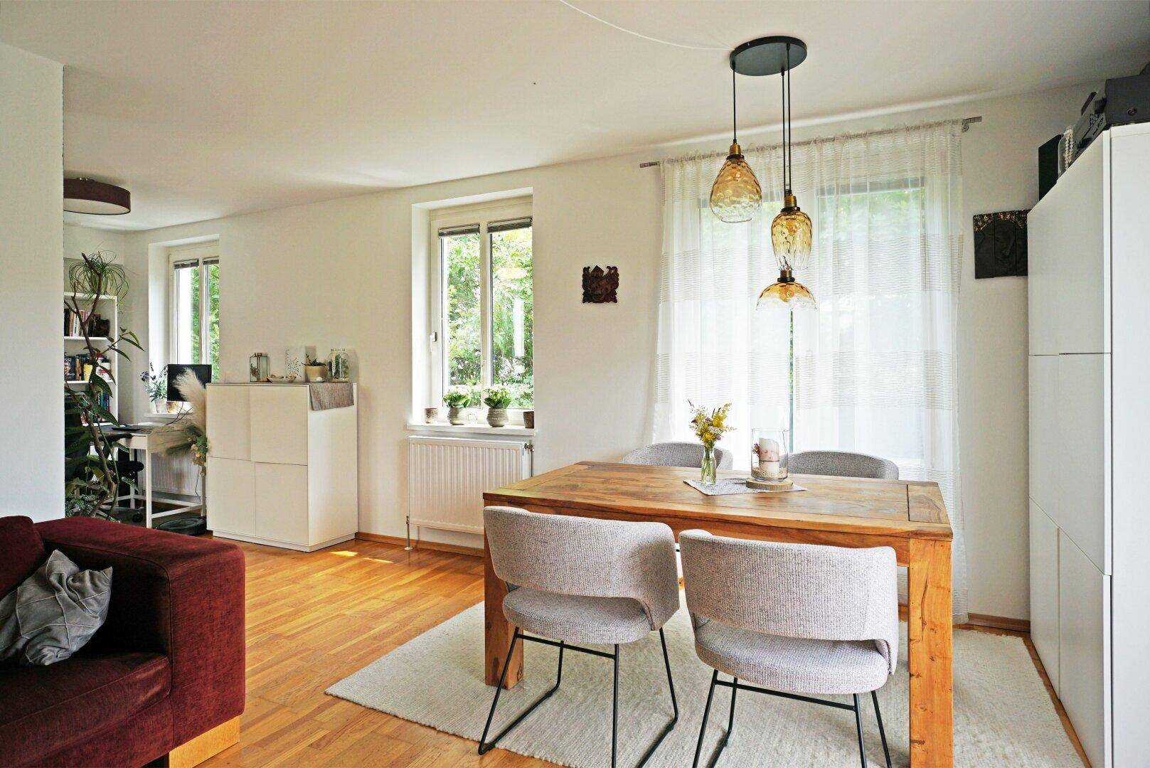 Gemütlicher Essbereich mit Holztisch, hellen Stühlen und Blick ins Grüne durch große Fenster.