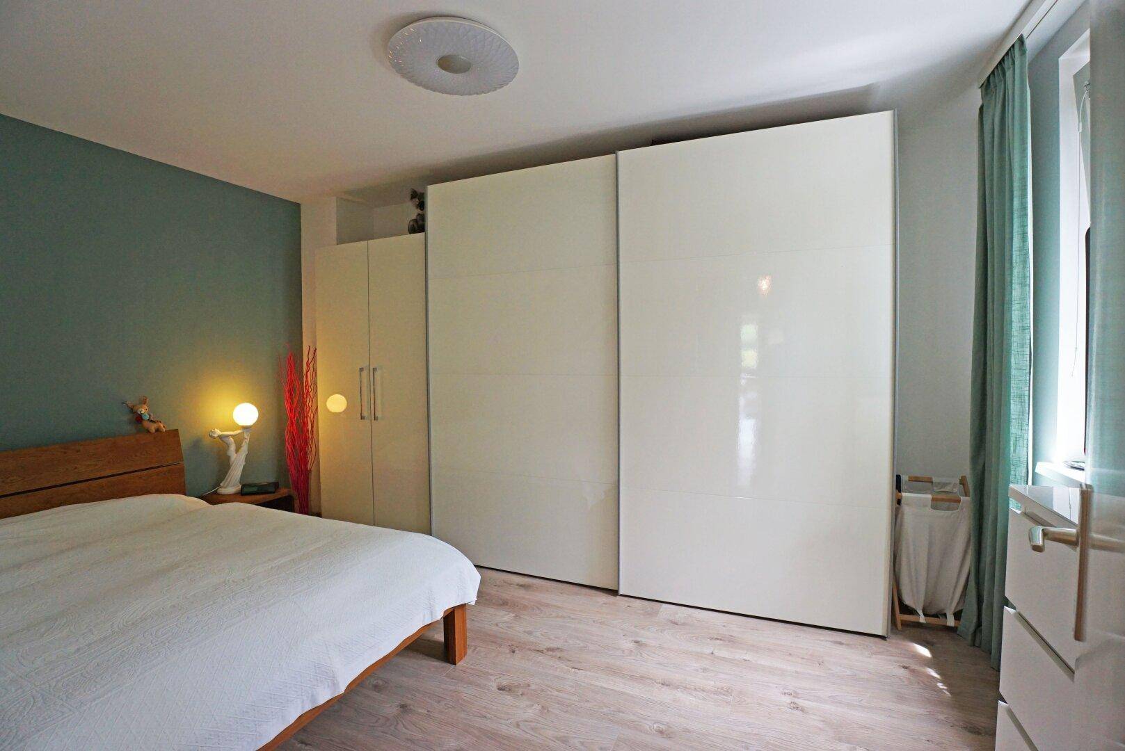 Helles Schlafzimmer mit Holzboden, großer weißer Schrankwand und grüner Akzentwand.