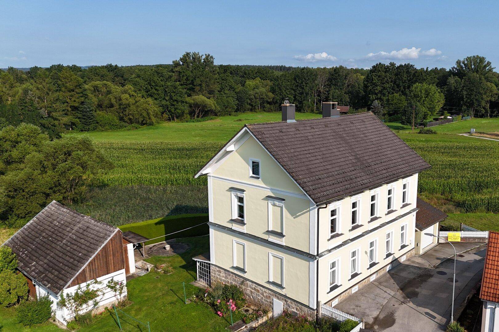 Luftaufnahme des Hauses mit angrenzenden Feldern und Wäldern unter blauem Himmel.