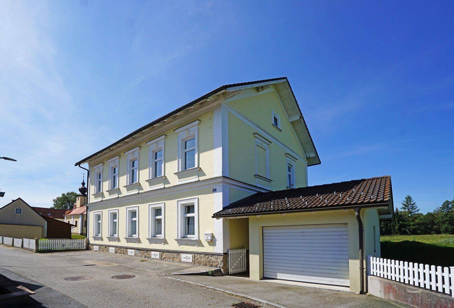 Ansicht des Hauses von der Straße mit einer Garage und einem weißen Zaun.