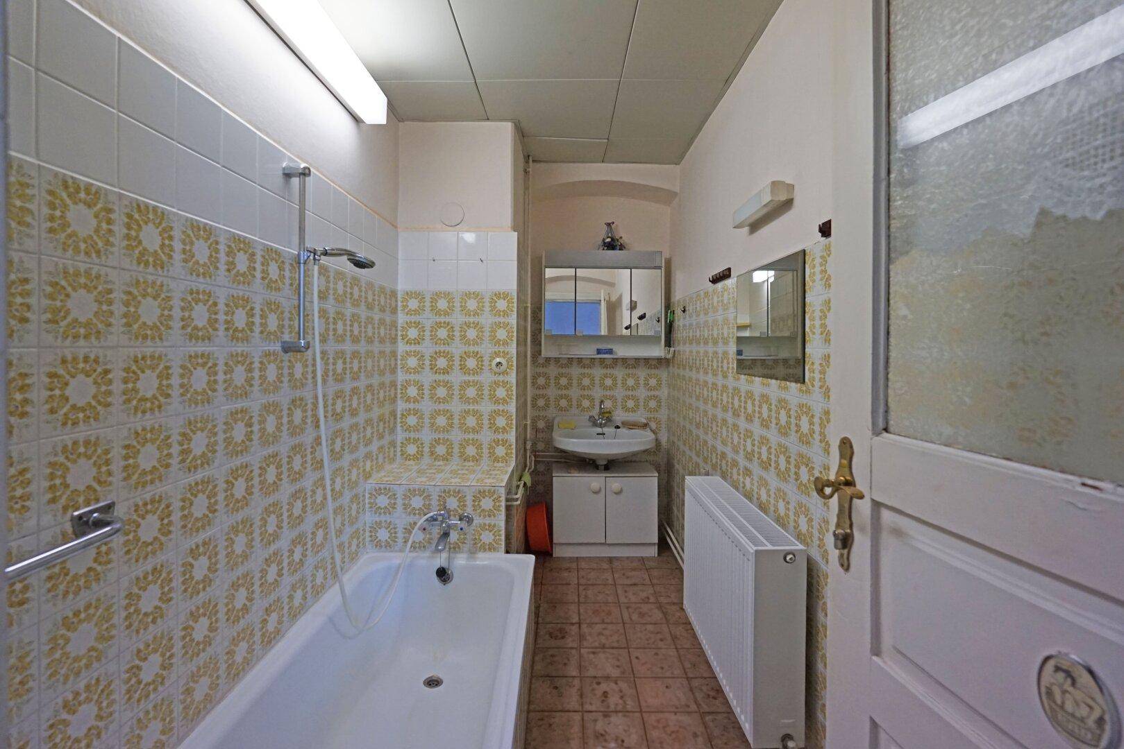 Badezimmer mit Badewanne, Waschbecken und gemusterten Fliesen im 80er-Jahre-Stil.