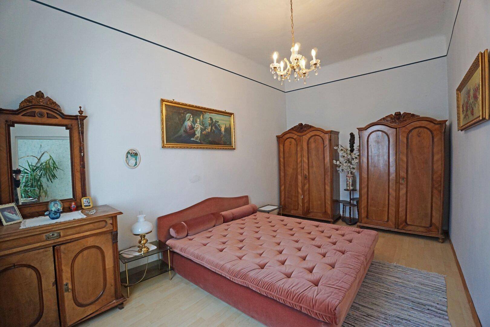 Schlafzimmer mit großem Bett, antiken Holzmöbeln und Kronleuchter.