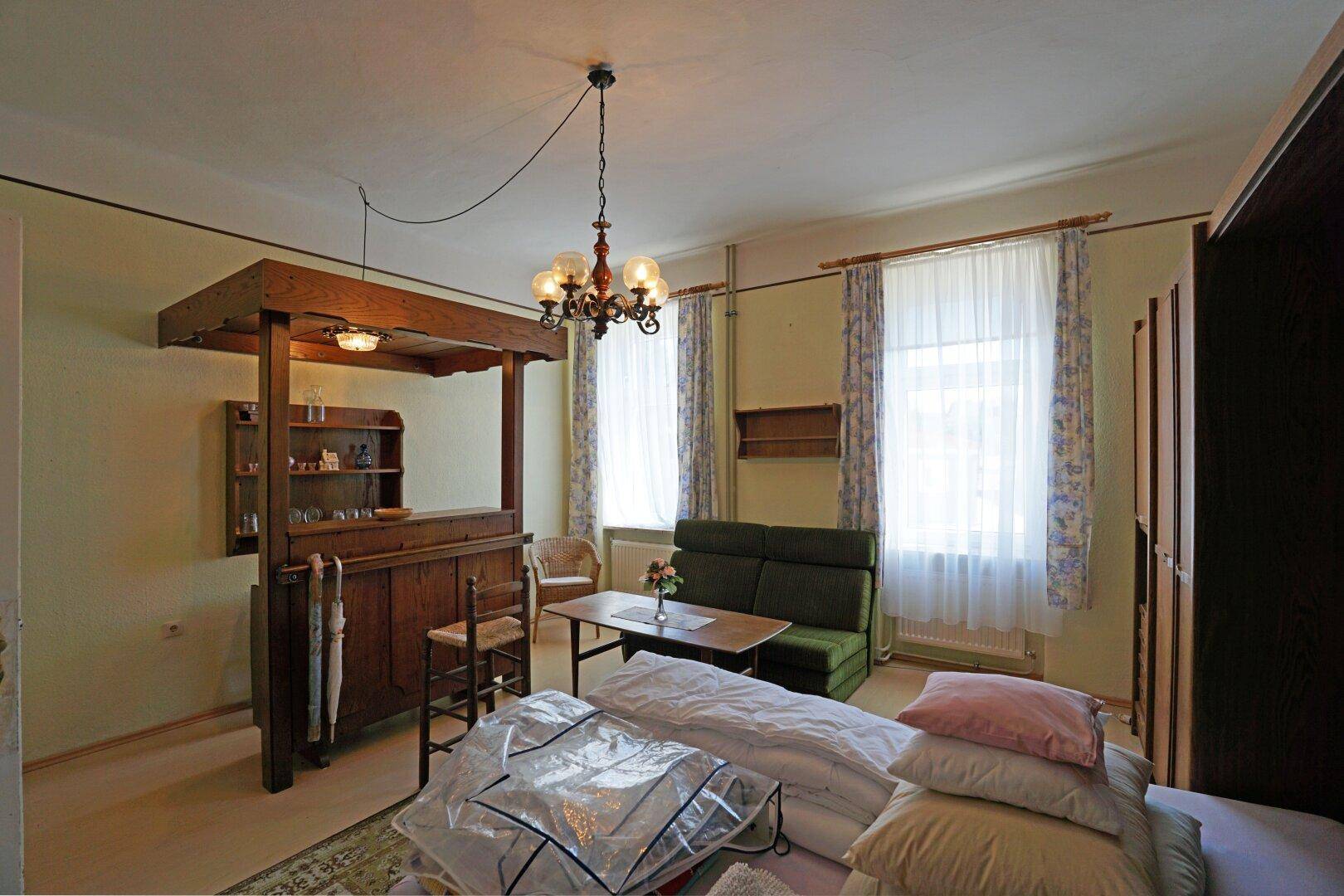 Schlafzimmer mit Bett, Sofa und einer Holzbar, die als Raumteiler dient.