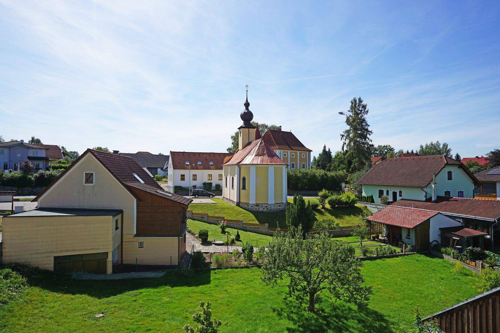 Malerische Ansicht eines Dorfes mit einer Kirche und grünen Gärten unter blauem Himmel.