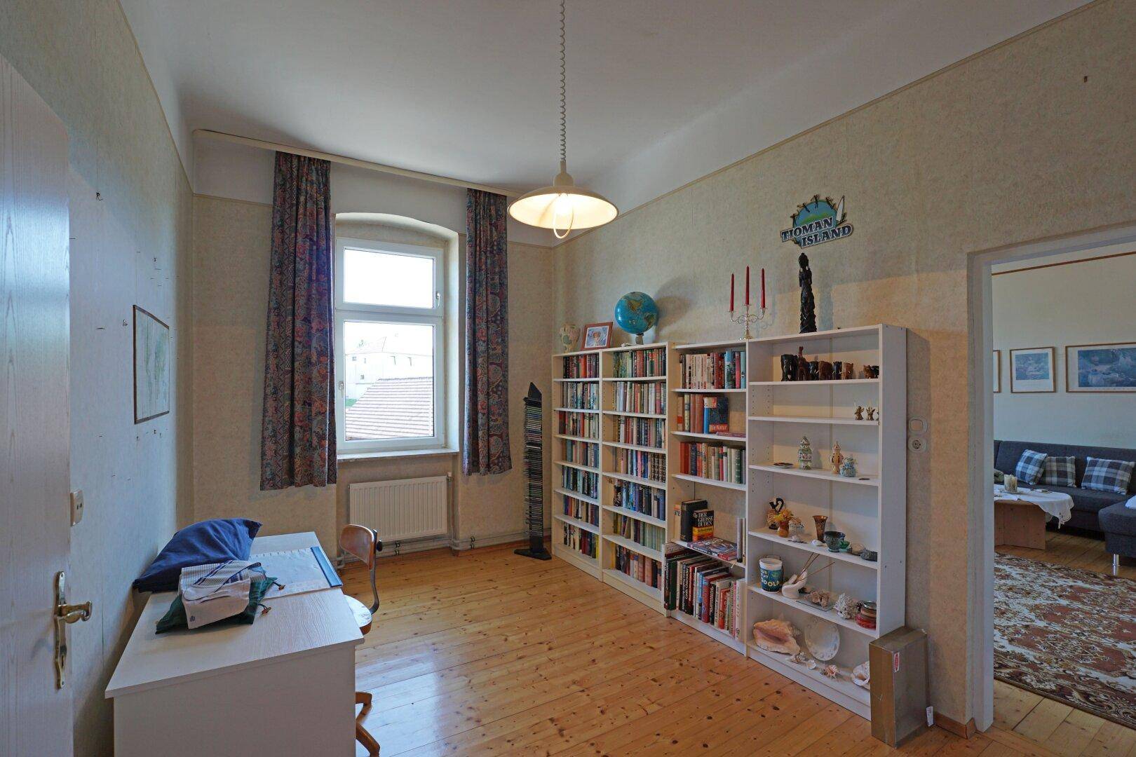 Arbeitszimmer mit Holzboden, Bücherregalen und einem Schreibtisch am Fenster.