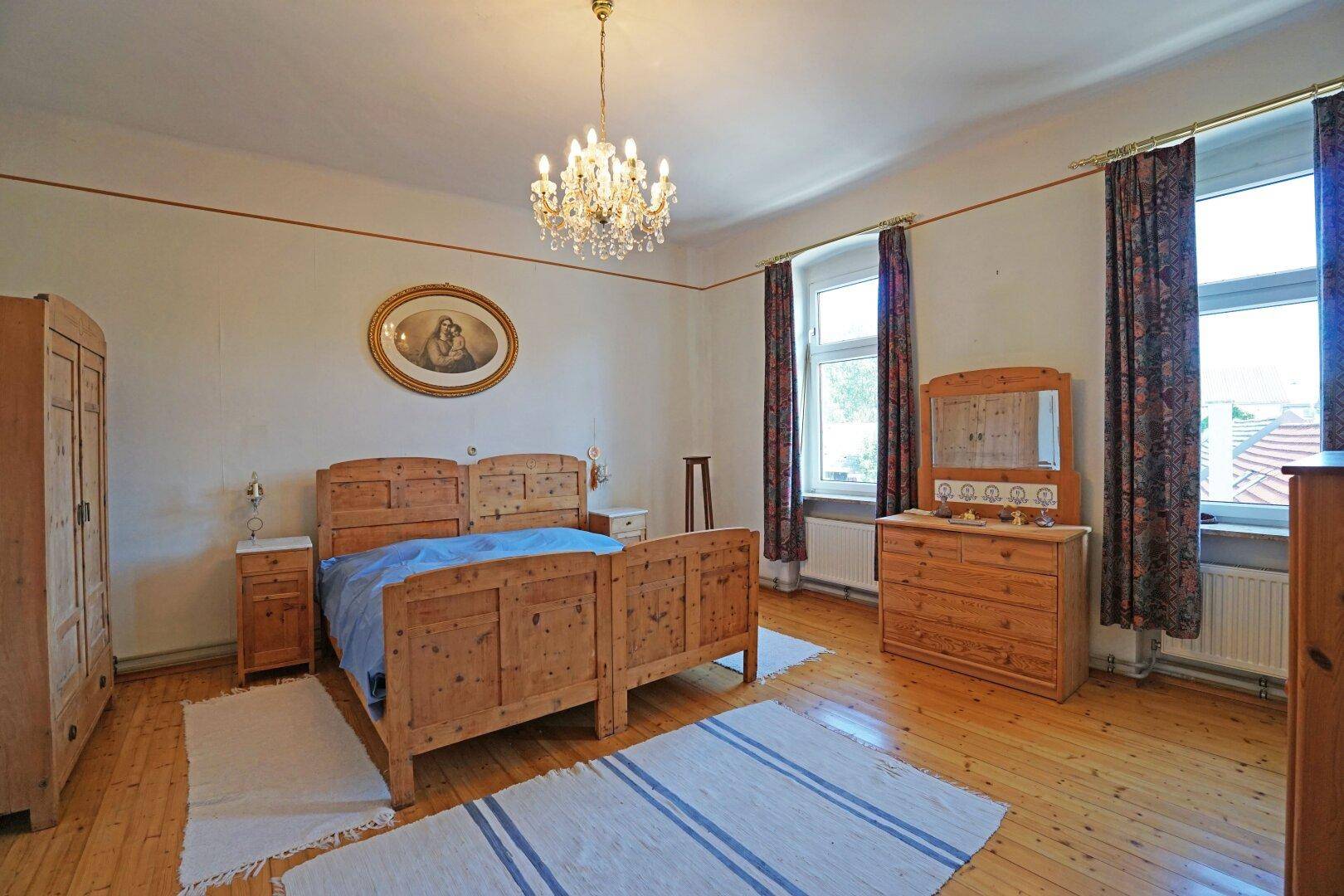 Schlafzimmer mit Holzbett, Kommode und Kronleuchter, hell und geräumig.