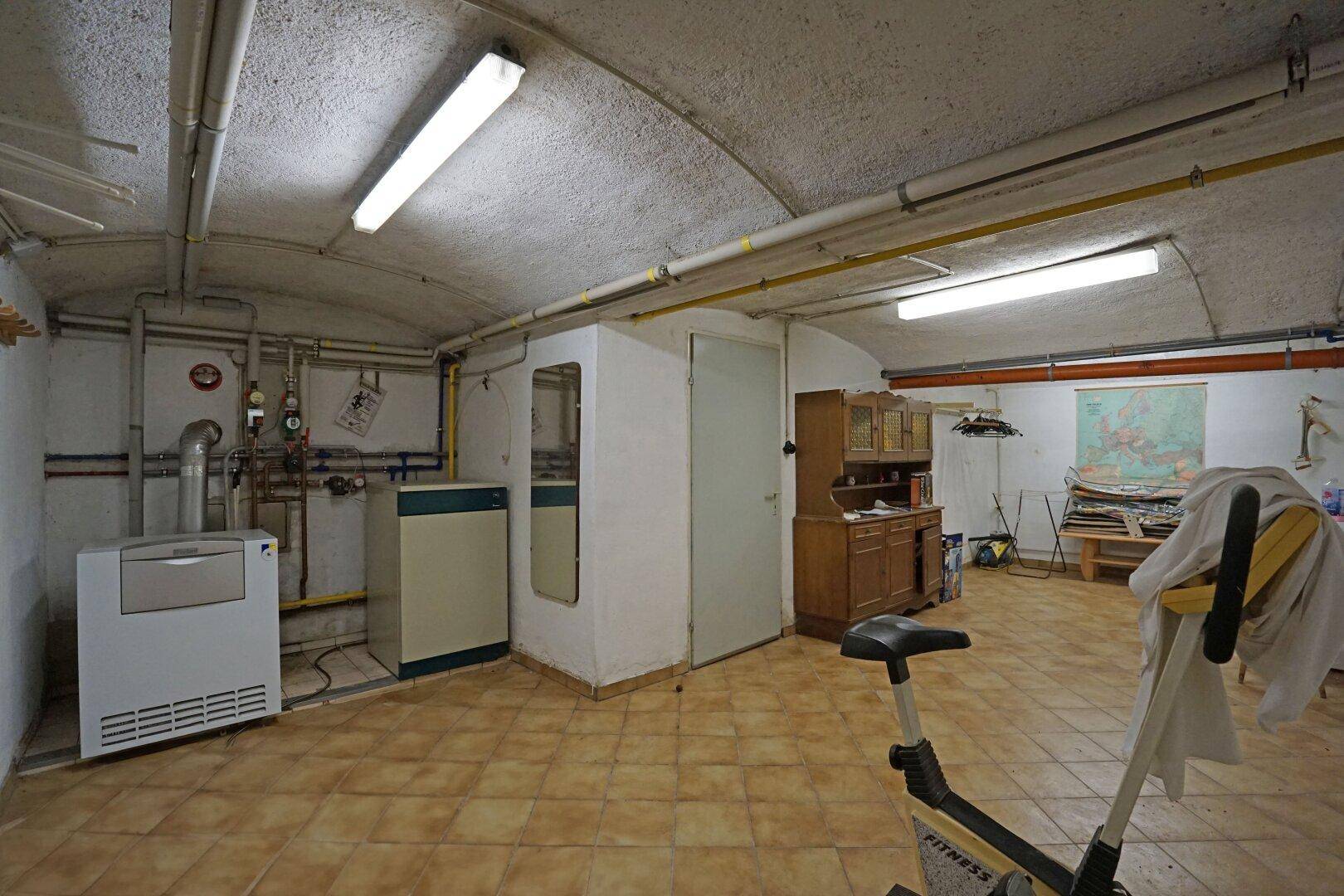 Geräumiger Kellerraum mit Heizungsanlage, Fliesenboden und Fitnessgerät.