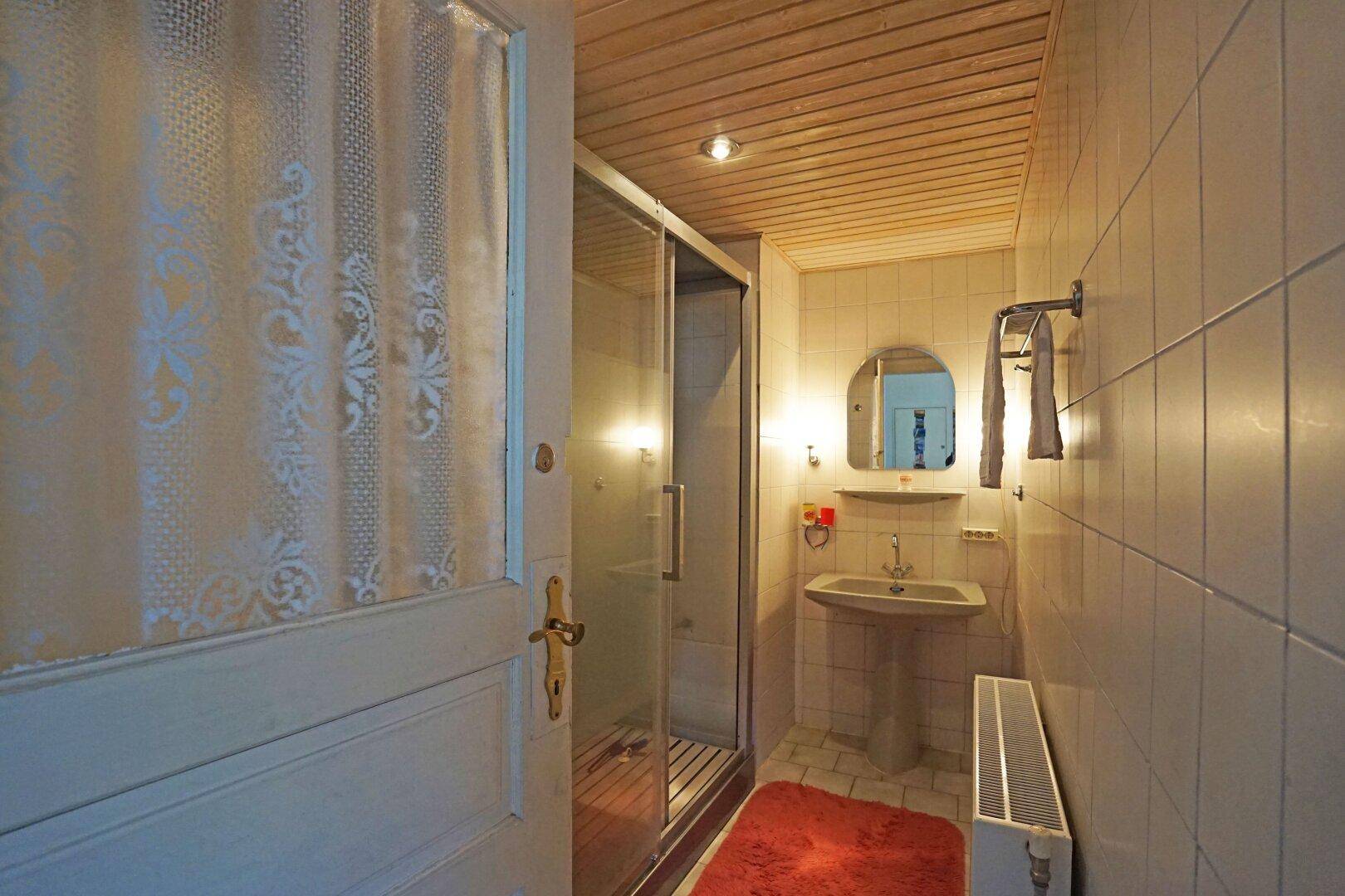 Kleines Badezimmer mit Duschkabine, Waschbecken und Holzdecke.
