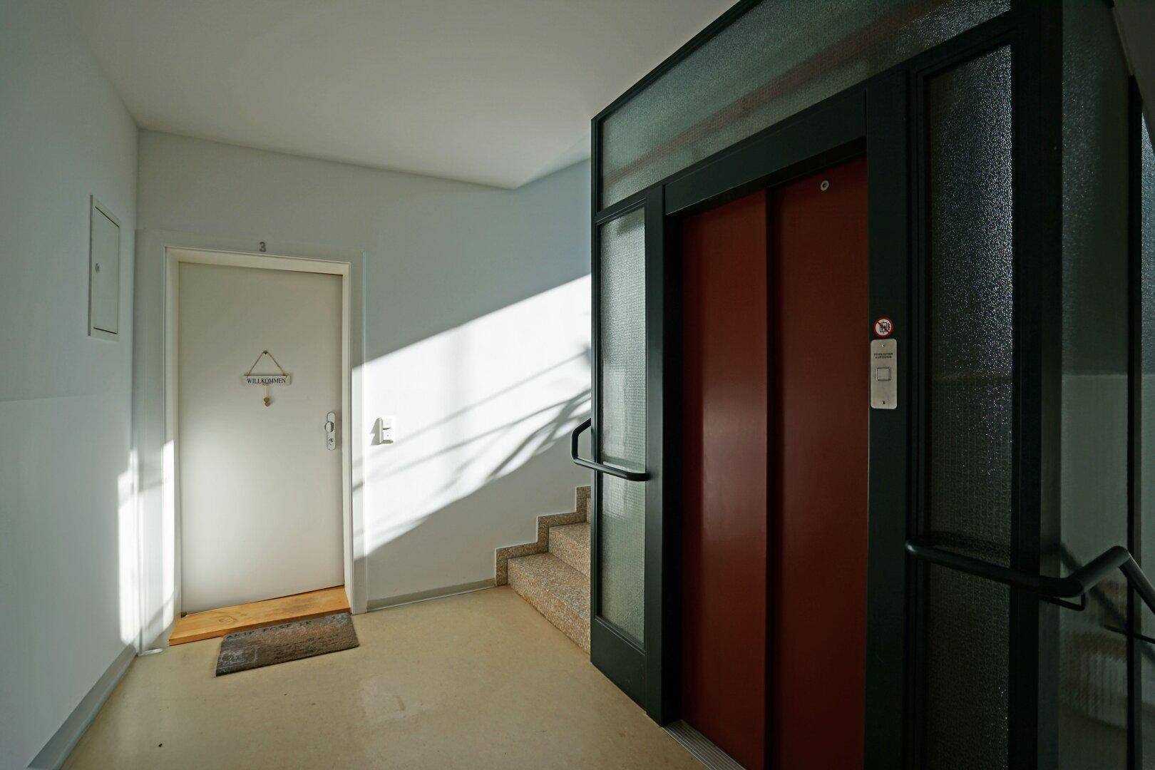 Heller Flur mit Aufzug und Treppenhaus, gut beleuchtet durch natürliches Licht.