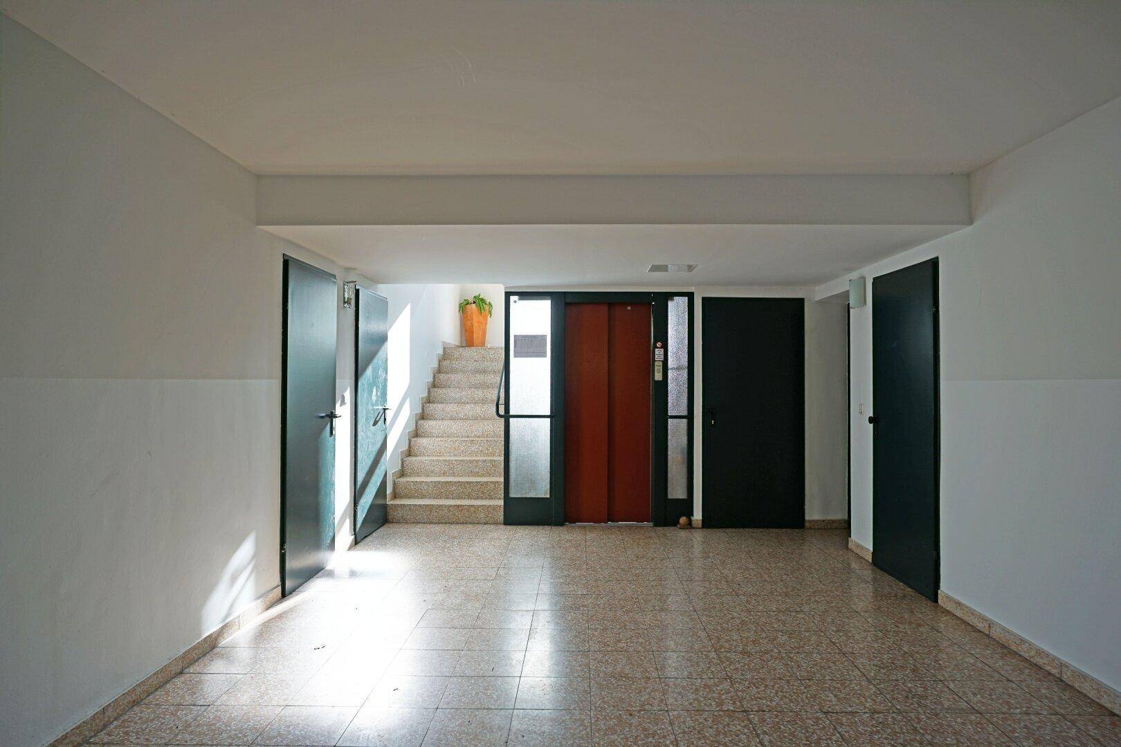 Geräumiger Eingangsbereich mit Fliesenboden, Treppe und Aufzug, der zu den Wohnungen führt.