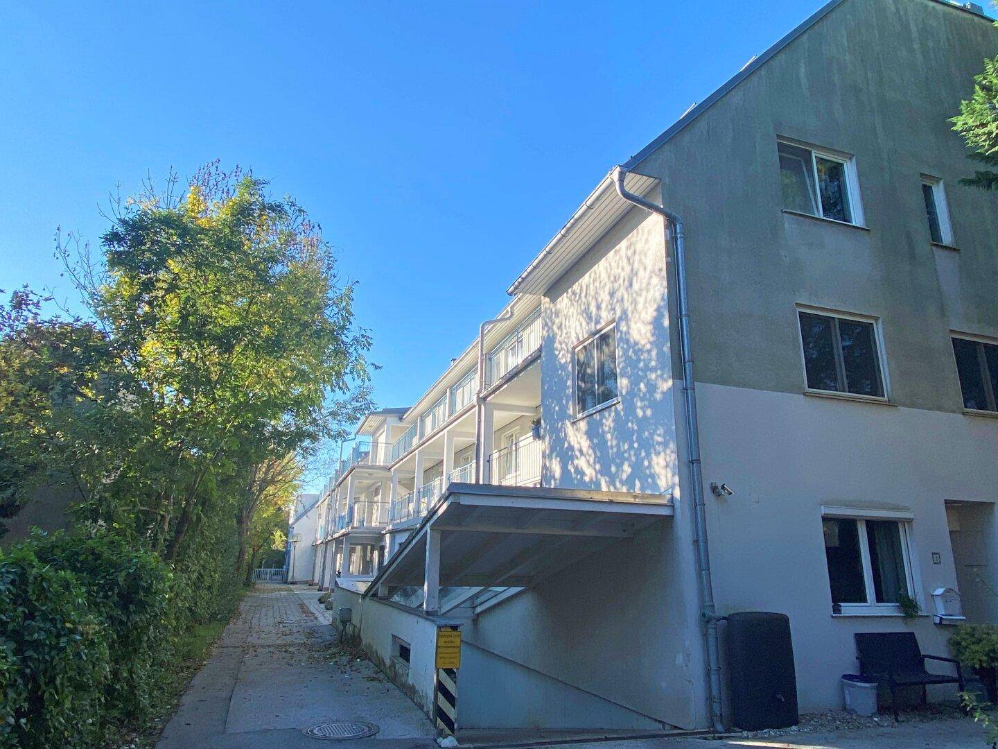Mehrfamilienhaus mit Balkonen und begrüntem Außenbereich unter blauem Himmel.