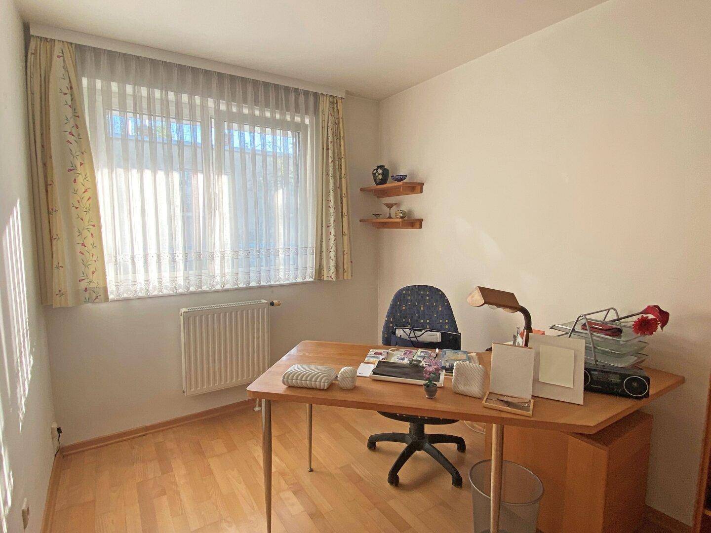 Helles Arbeitszimmer mit Holzschreibtisch, Parkettboden und großem Fenster.