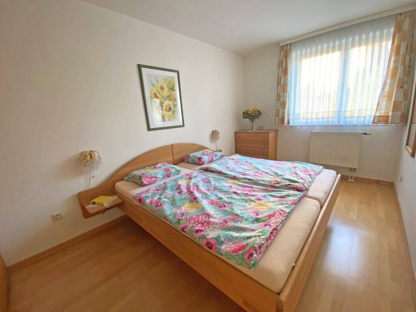 Freundliches Schlafzimmer mit Doppelbett, floraler Bettwäsche und Parkettboden.