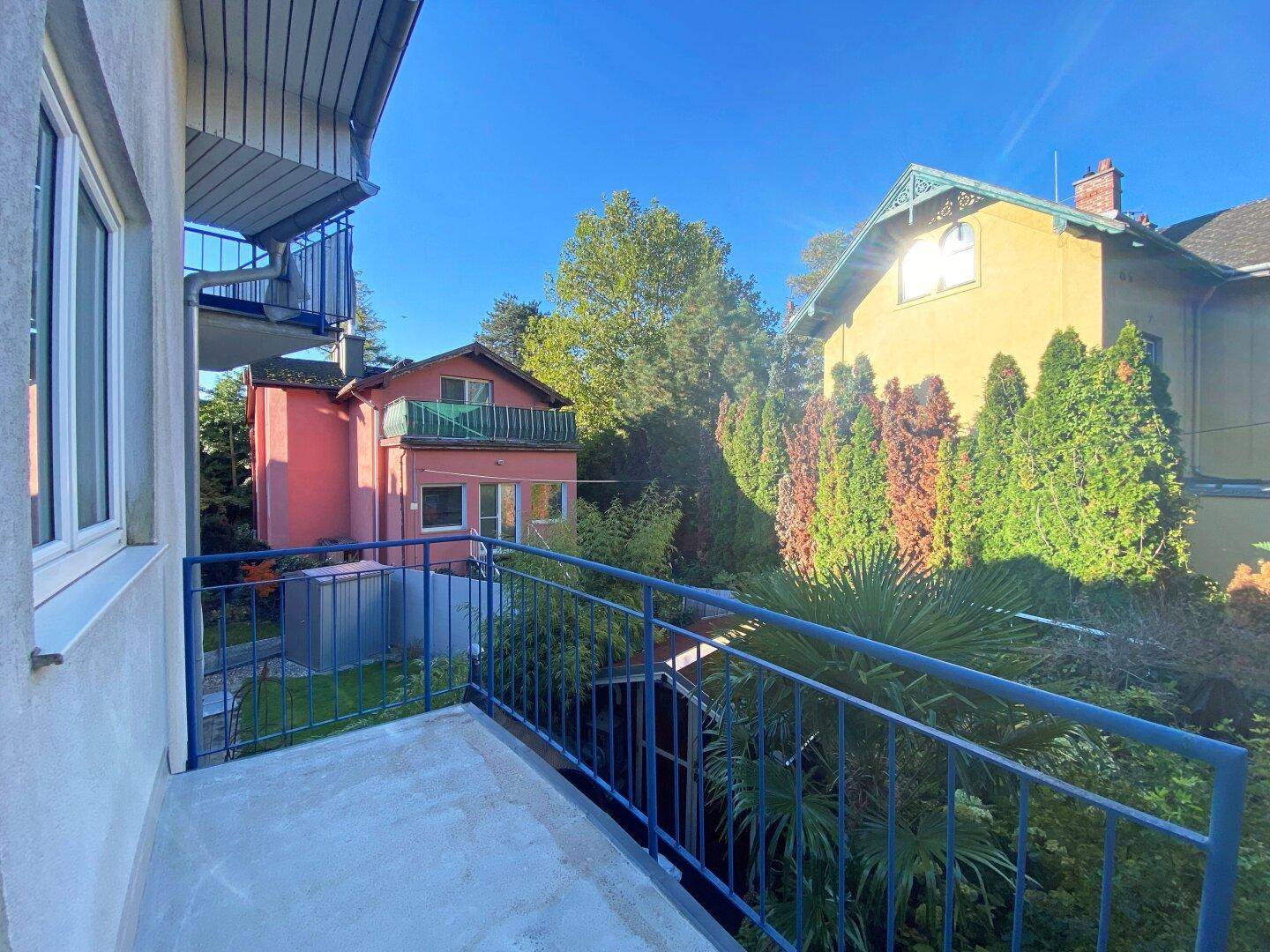 Balkon mit blauem Geländer und Blick auf grüne Gärten und Nachbarhäuser.