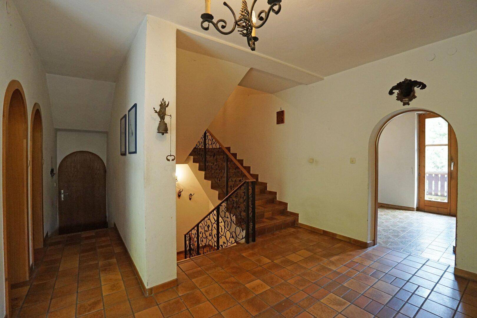 Geräumiger Flur mit Terrakotta-Fliesenboden und einer geschwungenen Treppe mit schmiedeeisernem Geländer.