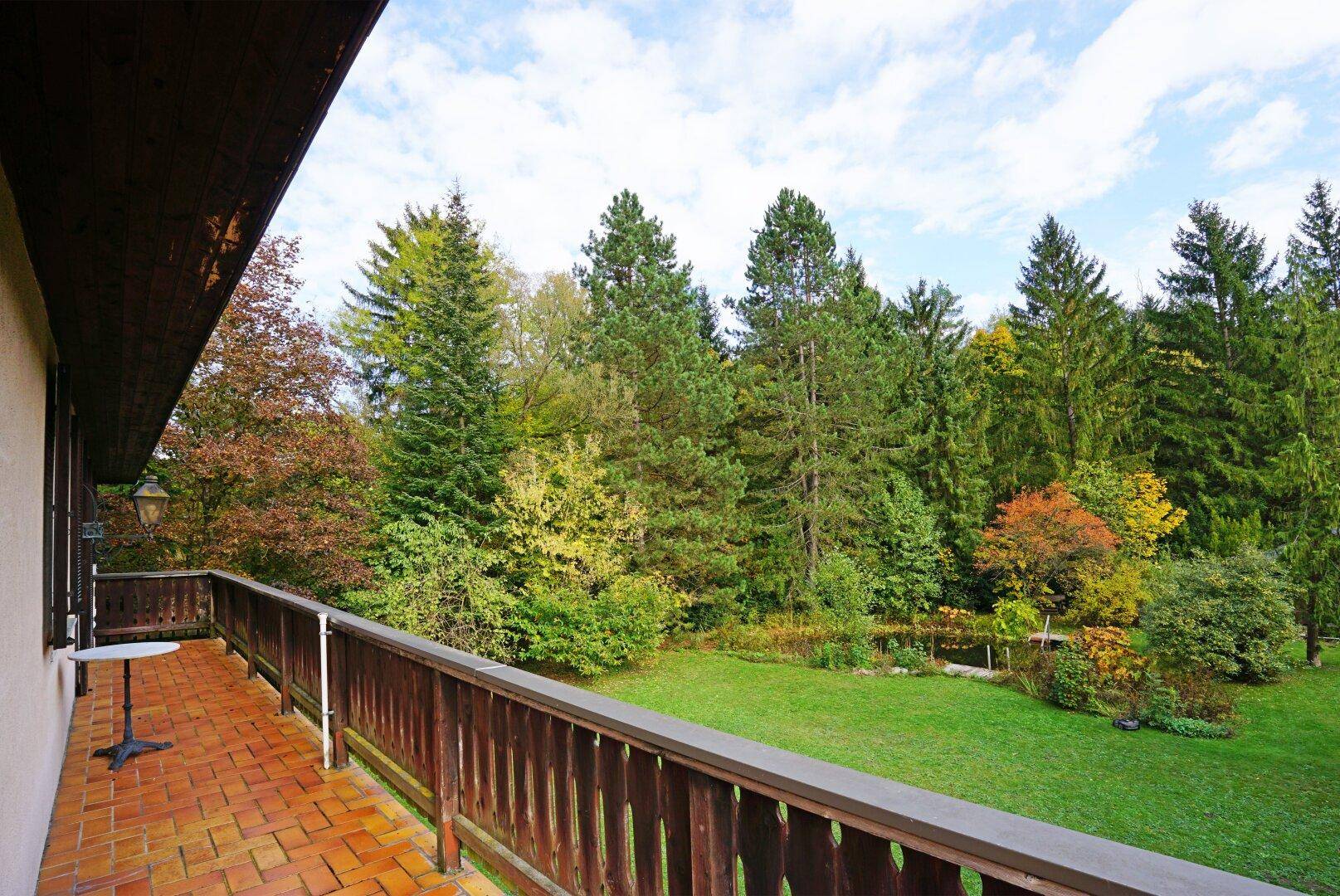 Geräumiger Balkon mit Terrakotta-Fliesen und Holzgeländer, bietet Blick auf den grünen Garten.