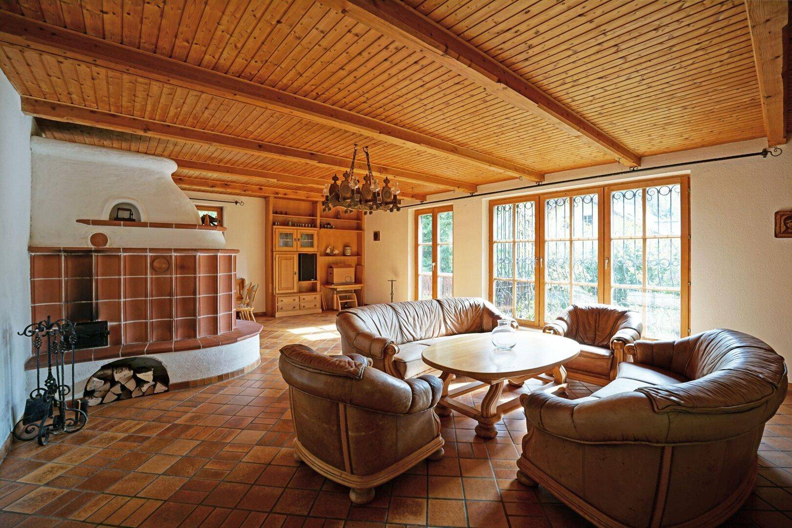 Gemütliches Wohnzimmer mit traditionellem Kachelofen, Holzbalkendecke und Terrakotta-Fliesenboden.