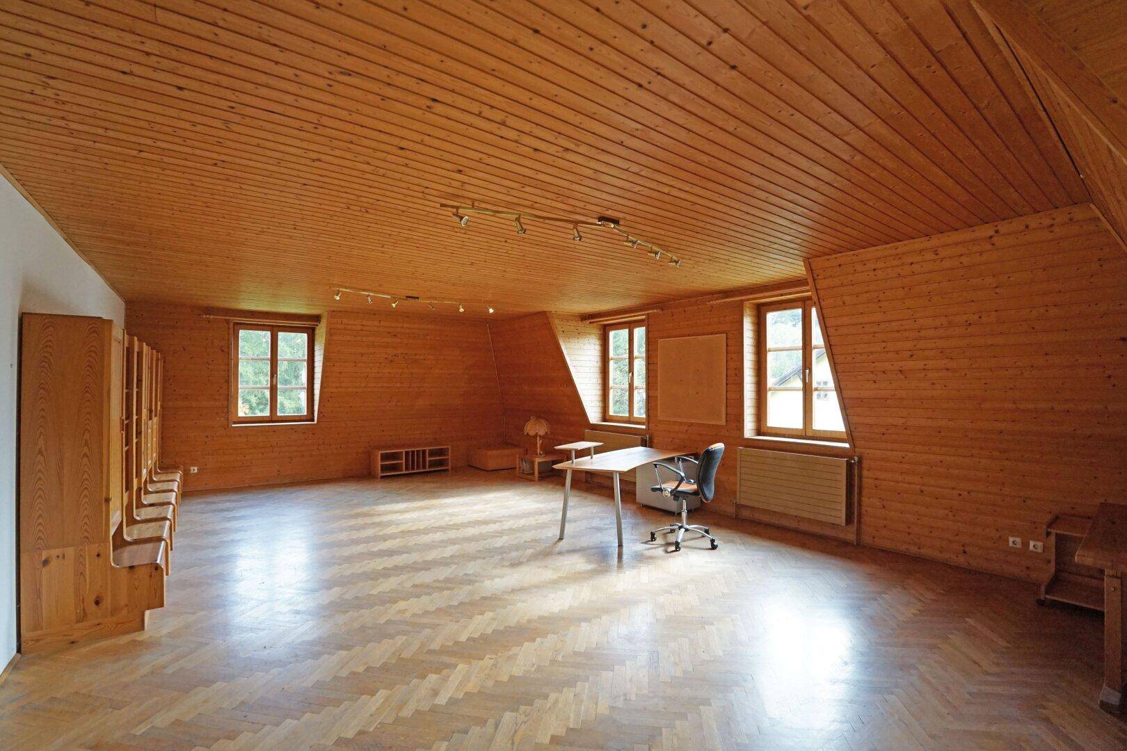 Helles Dachgeschosszimmer mit Holzverkleidung, Parkettboden und schrägen Wänden.