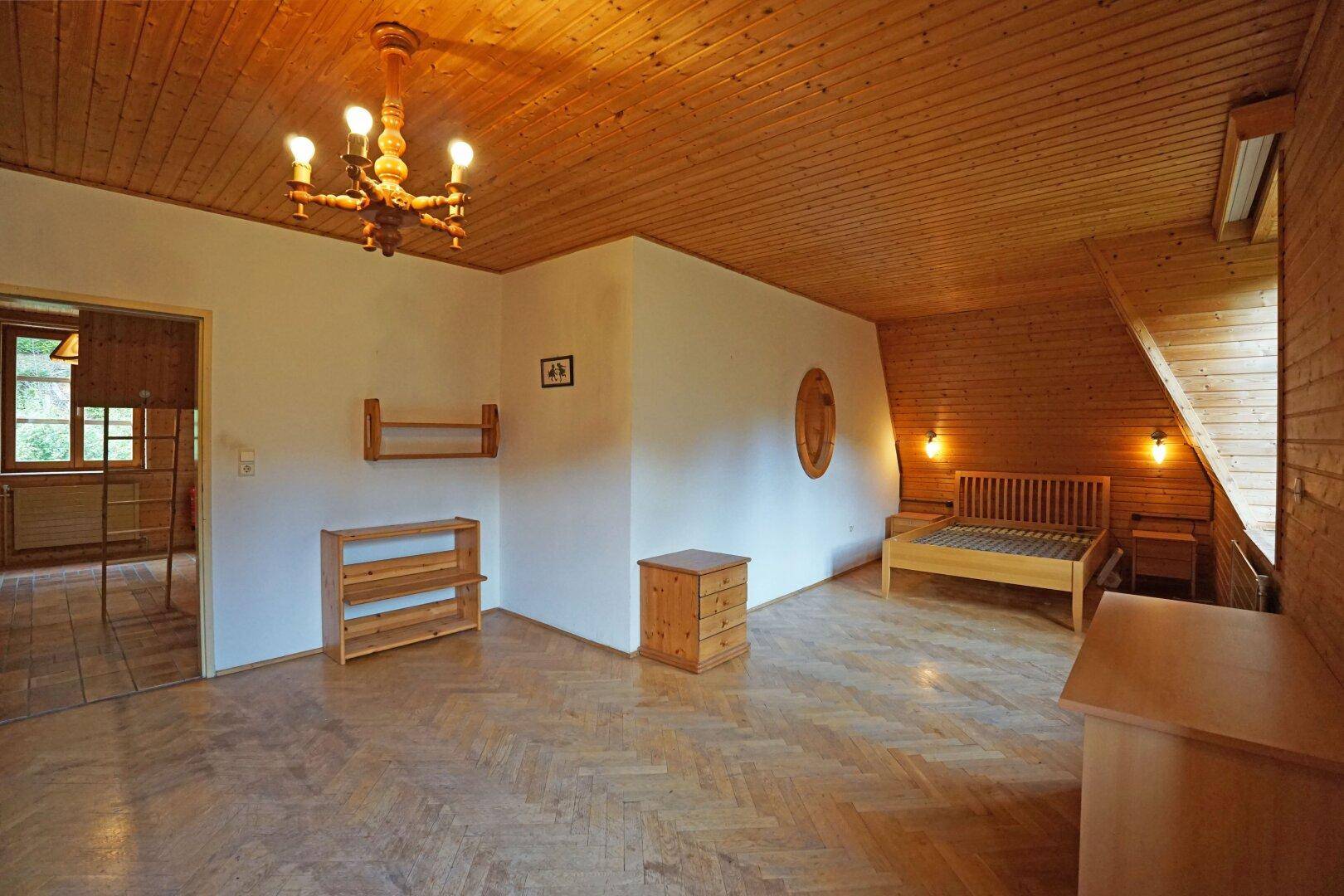 Gemütliches Schlafzimmer im Dachgeschoss mit Holzverkleidung, Parkettboden und schrägen Wänden.