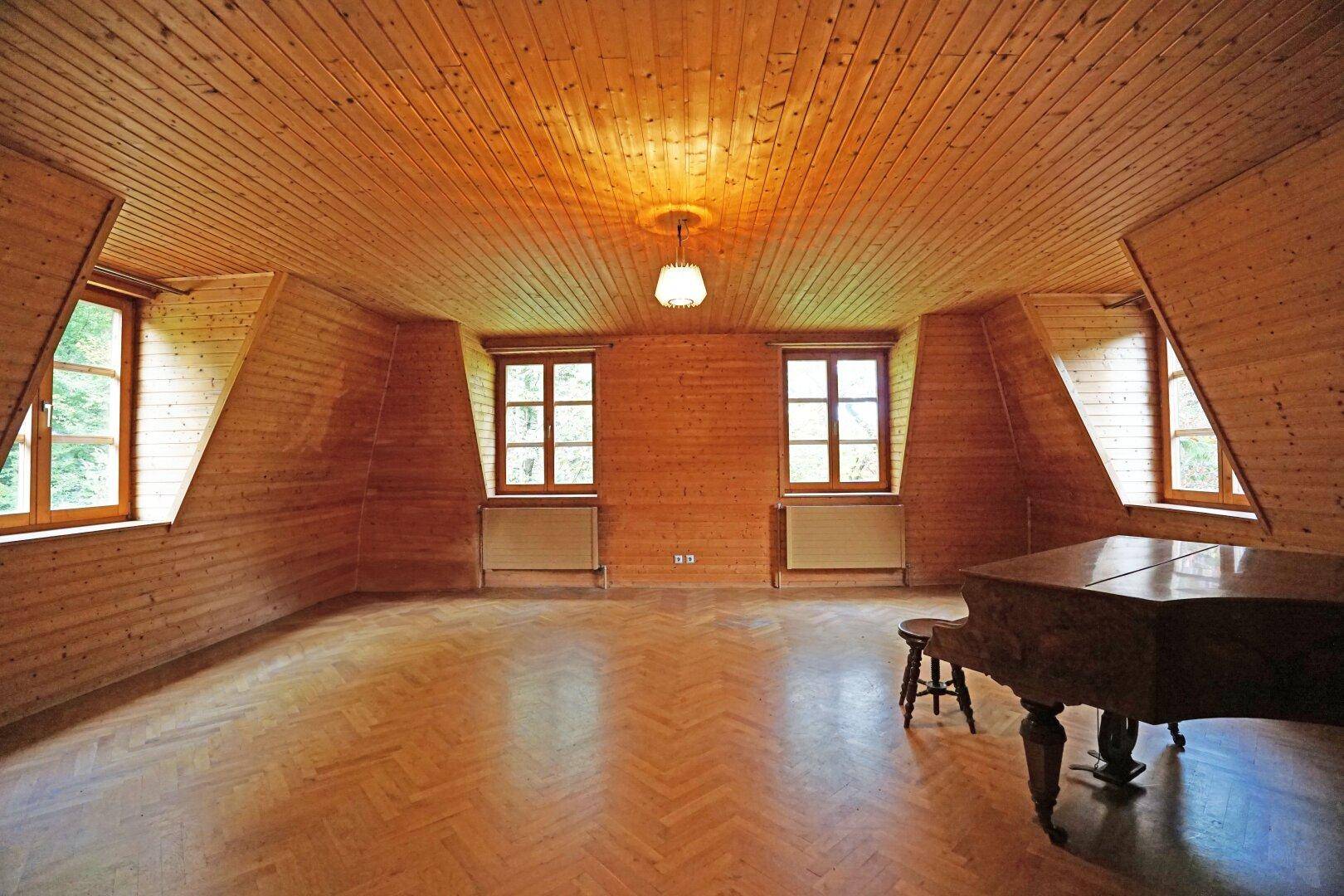 Geräumiges Zimmer im Dachgeschoss mit Holzverkleidung, Parkettboden und schrägen Wänden.