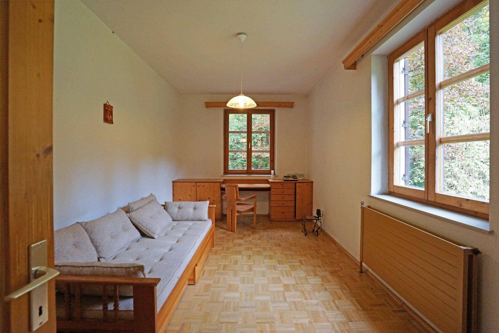 Kleines Zimmer mit Parkettboden, Holzmöbeln und Blick ins Grüne.