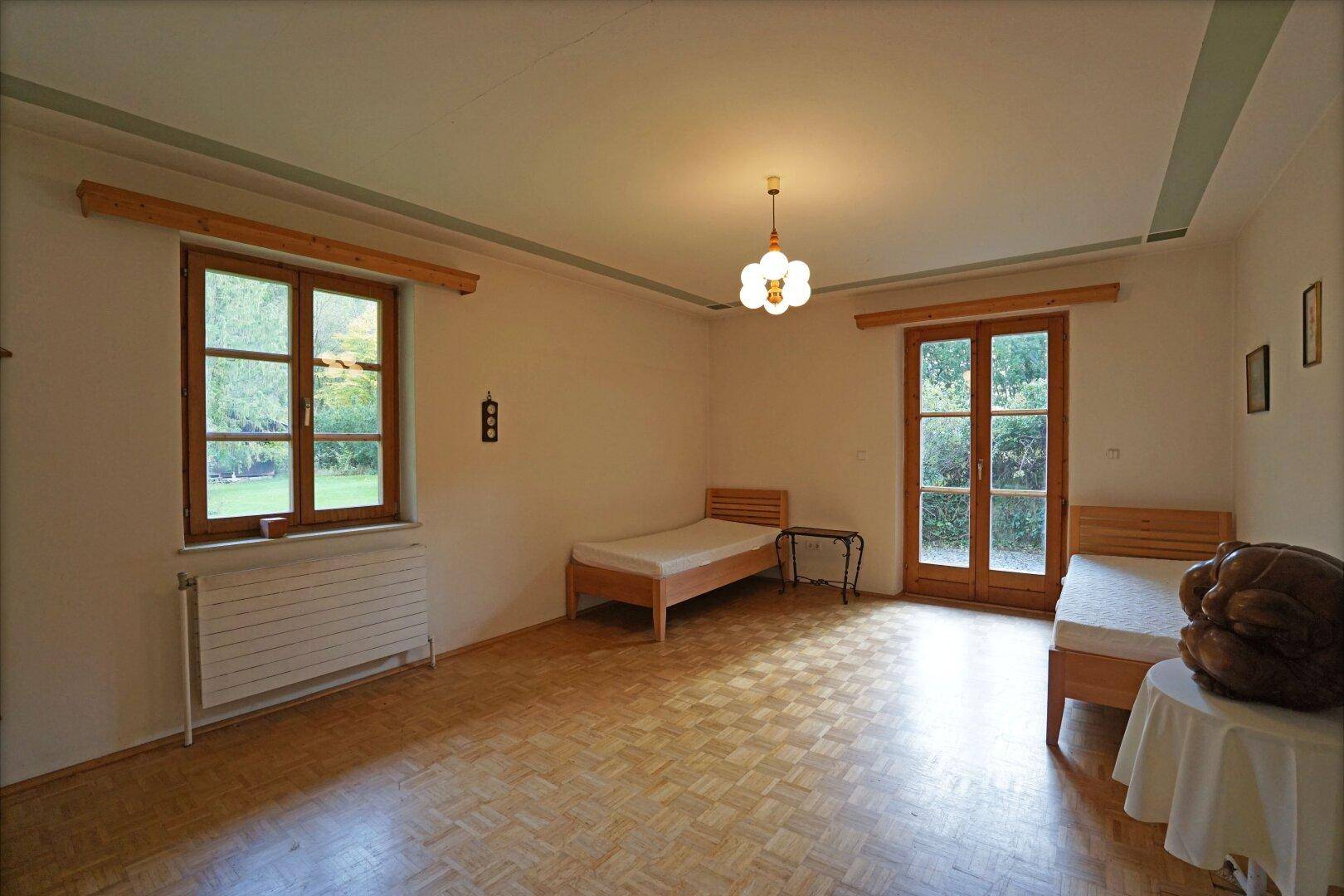 Helles Schlafzimmer mit Parkettboden, zwei Einzelbetten und Zugang zum Garten.
