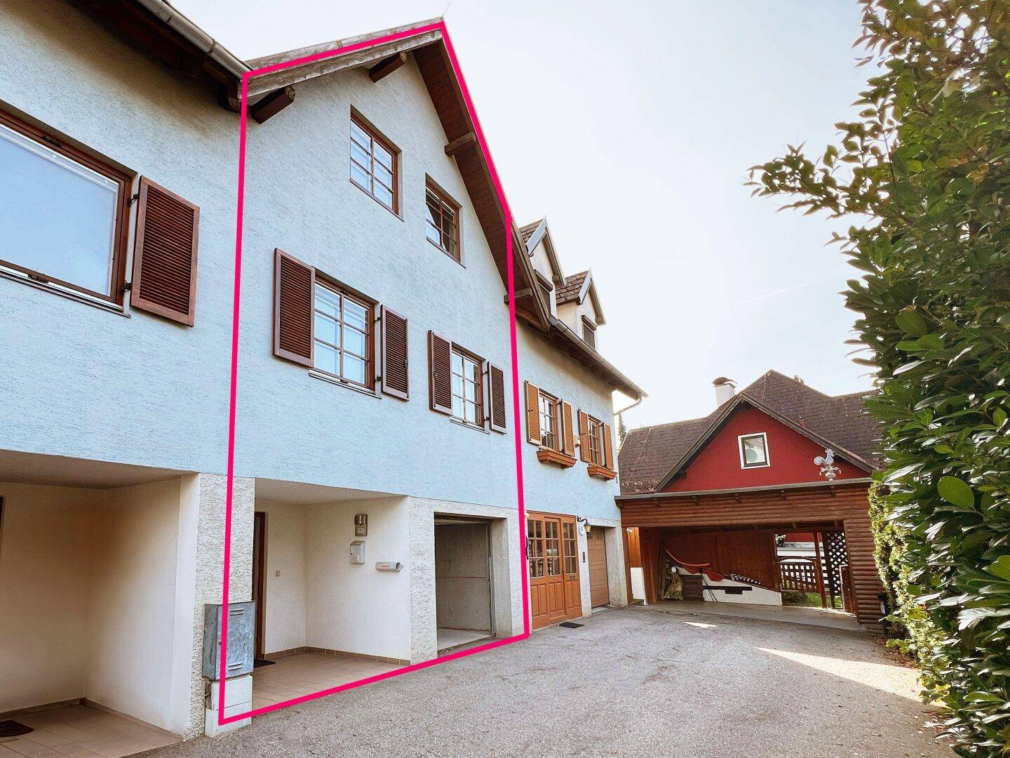 Gesamtansicht des Gebäudes mit Garagen, Carport und Zufahrt, umrahmt von einer pinken Linie.